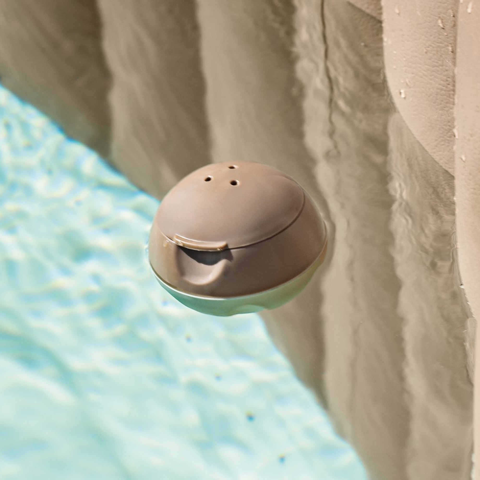 Runder, beiger, schwimmender Poolreiniger in blauem Wasser, brauner Poolrand.