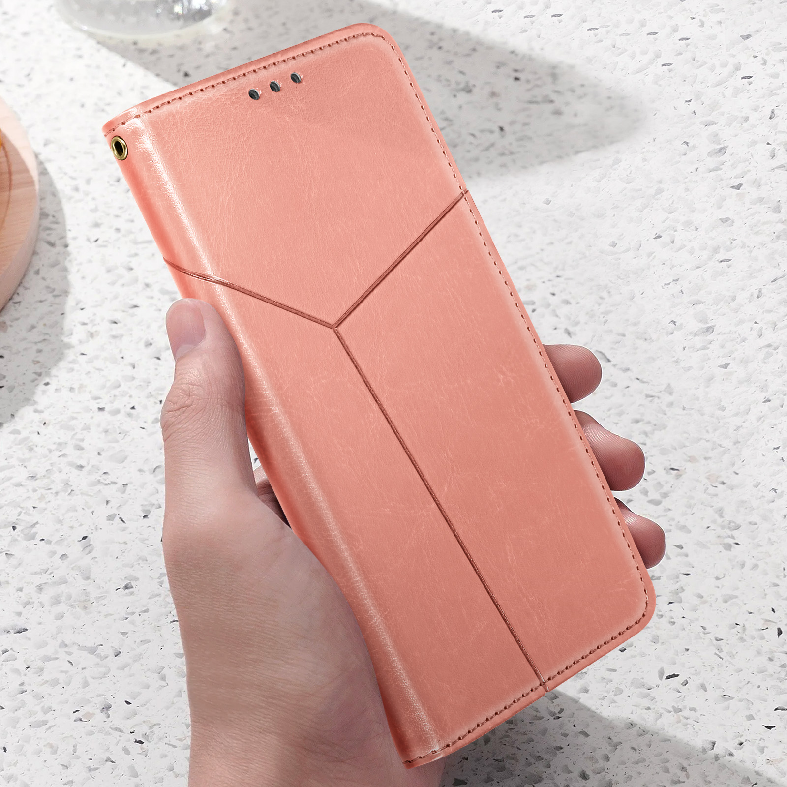 Persona che tiene una custodia per telefono color pesca con cuciture geometriche.