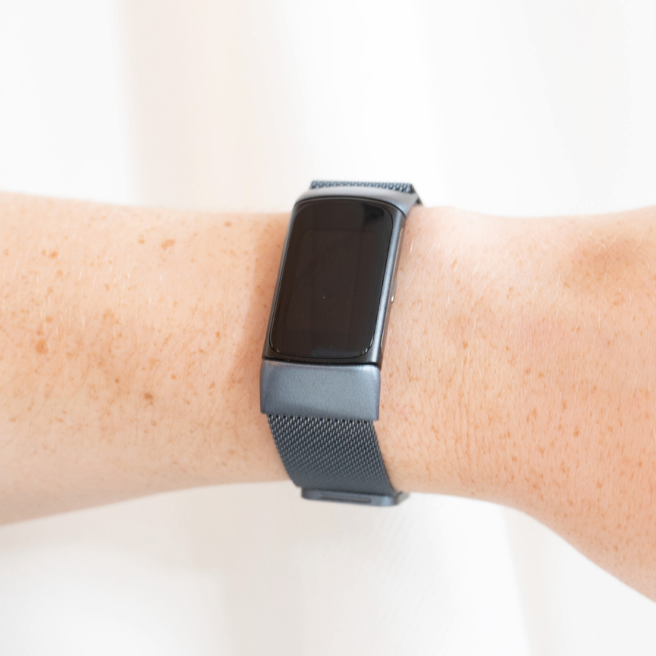 Handgelenk mit schwarzem Fitnesstracker, weißer Hintergrund.