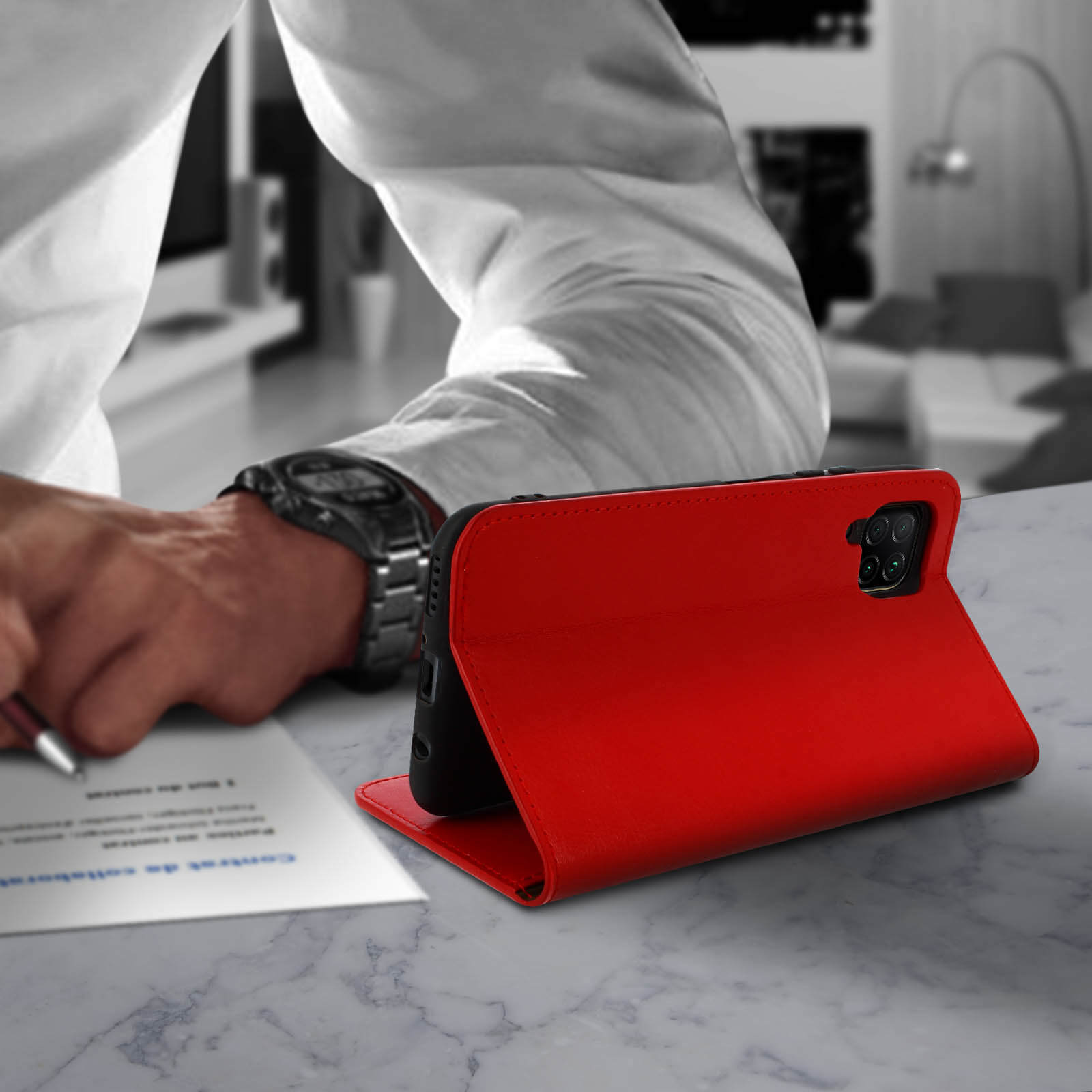 Custodia rossa per telefono aperta su un tavolo, persona che scrive sullo sfondo.