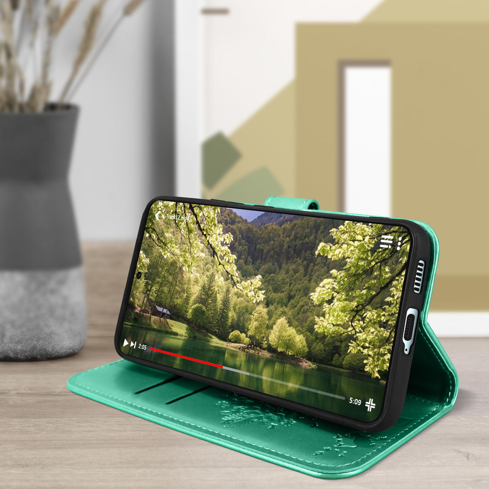 Un telefono mostra un video di un lago e una foresta, in una custodia verde.