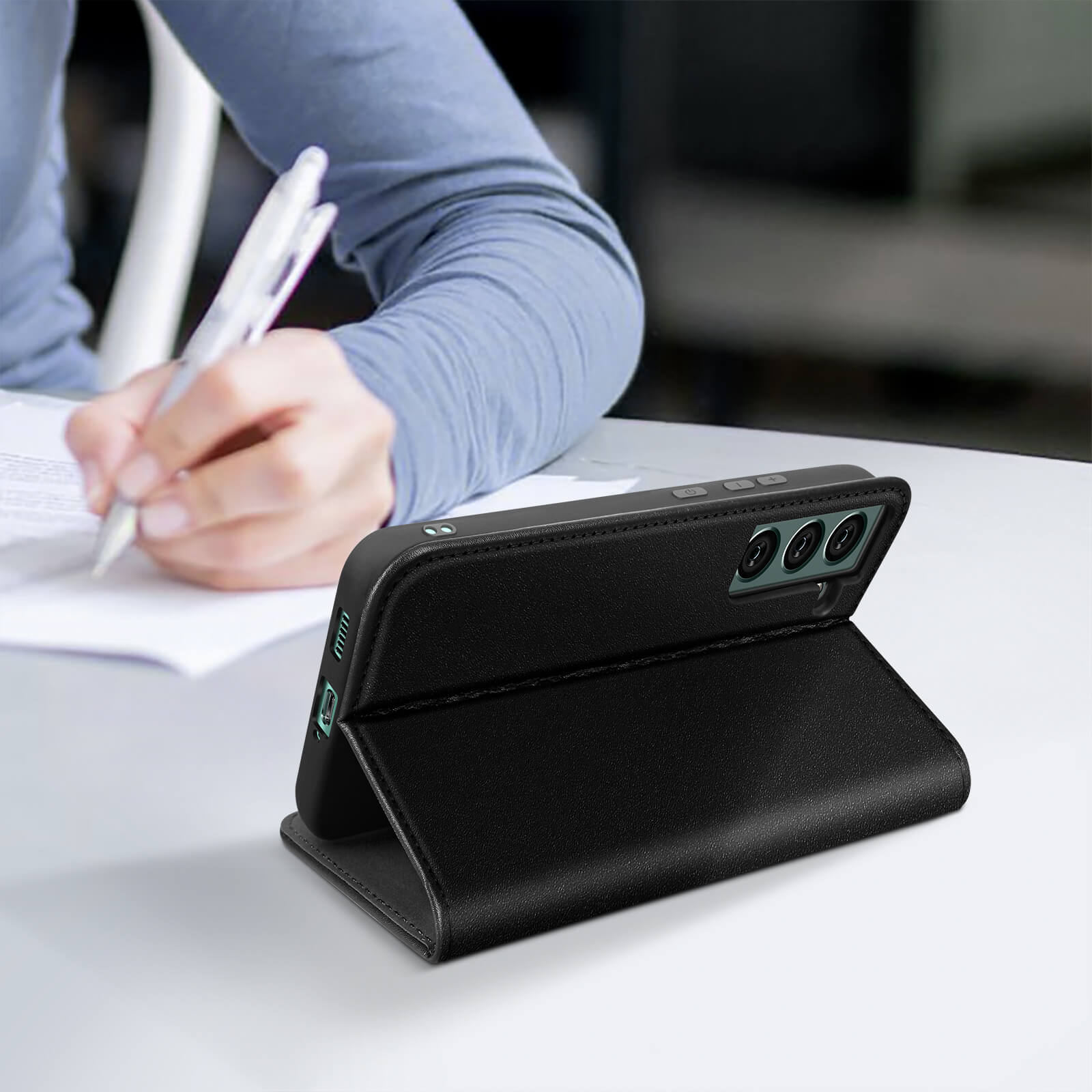 Étui de téléphone noir avec téléphone à l'intérieur. Sur une table blanche. Personne écrivant.