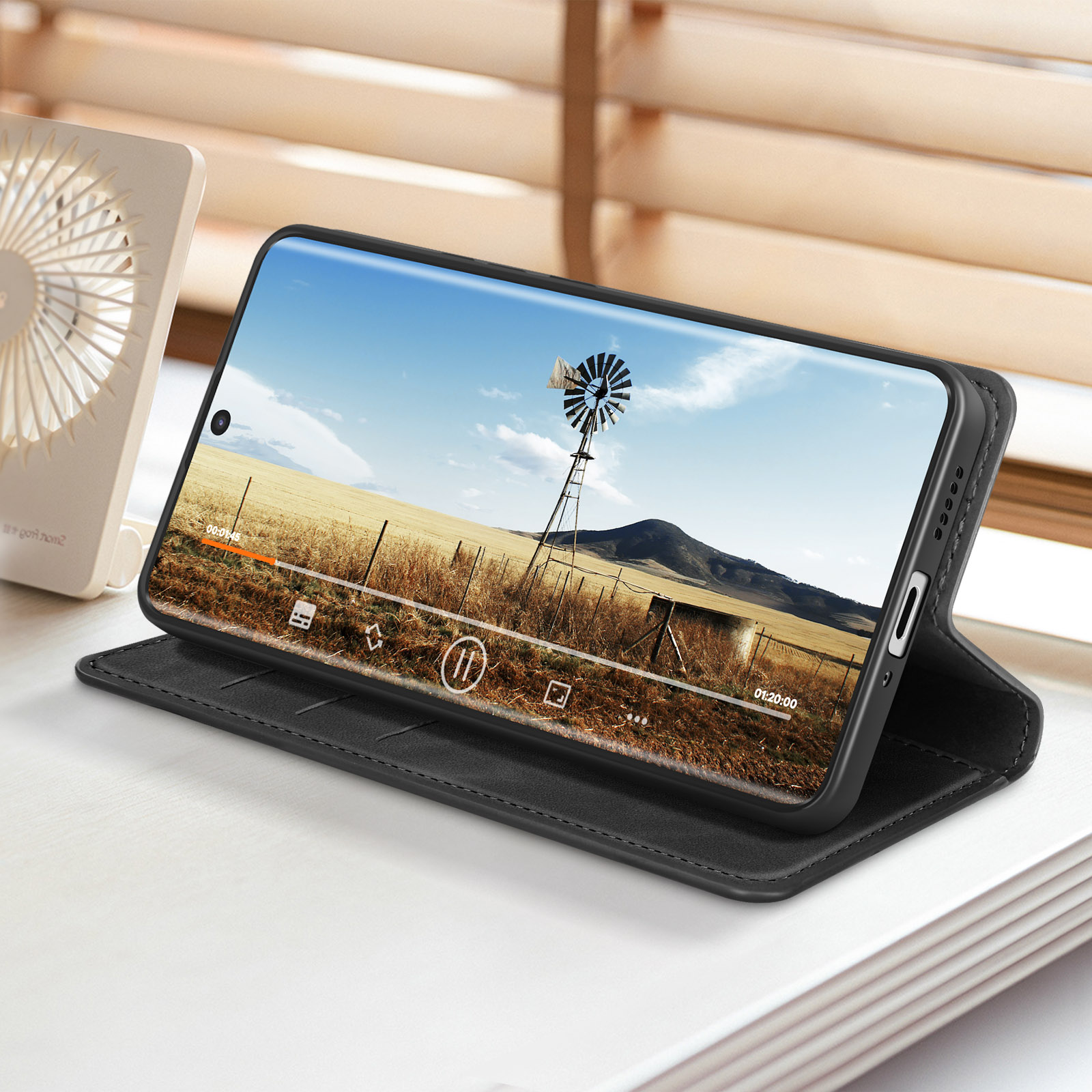 Telefono con video in riproduzione su custodia nera. Mostra un mulino a vento.