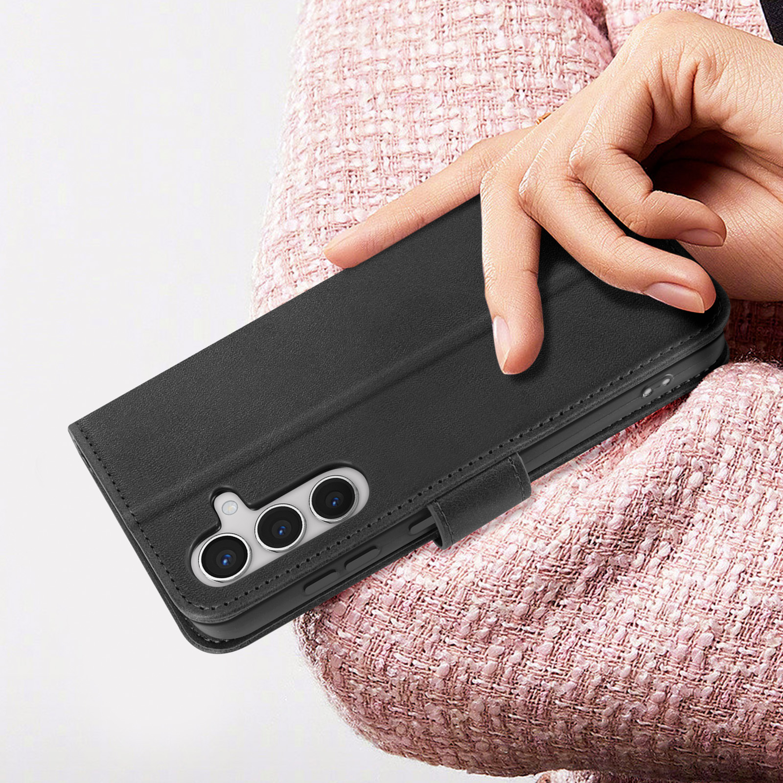 Hand hält eine geschlossene schwarze Handyhülle. Pinkes Hemd im Hintergrund.