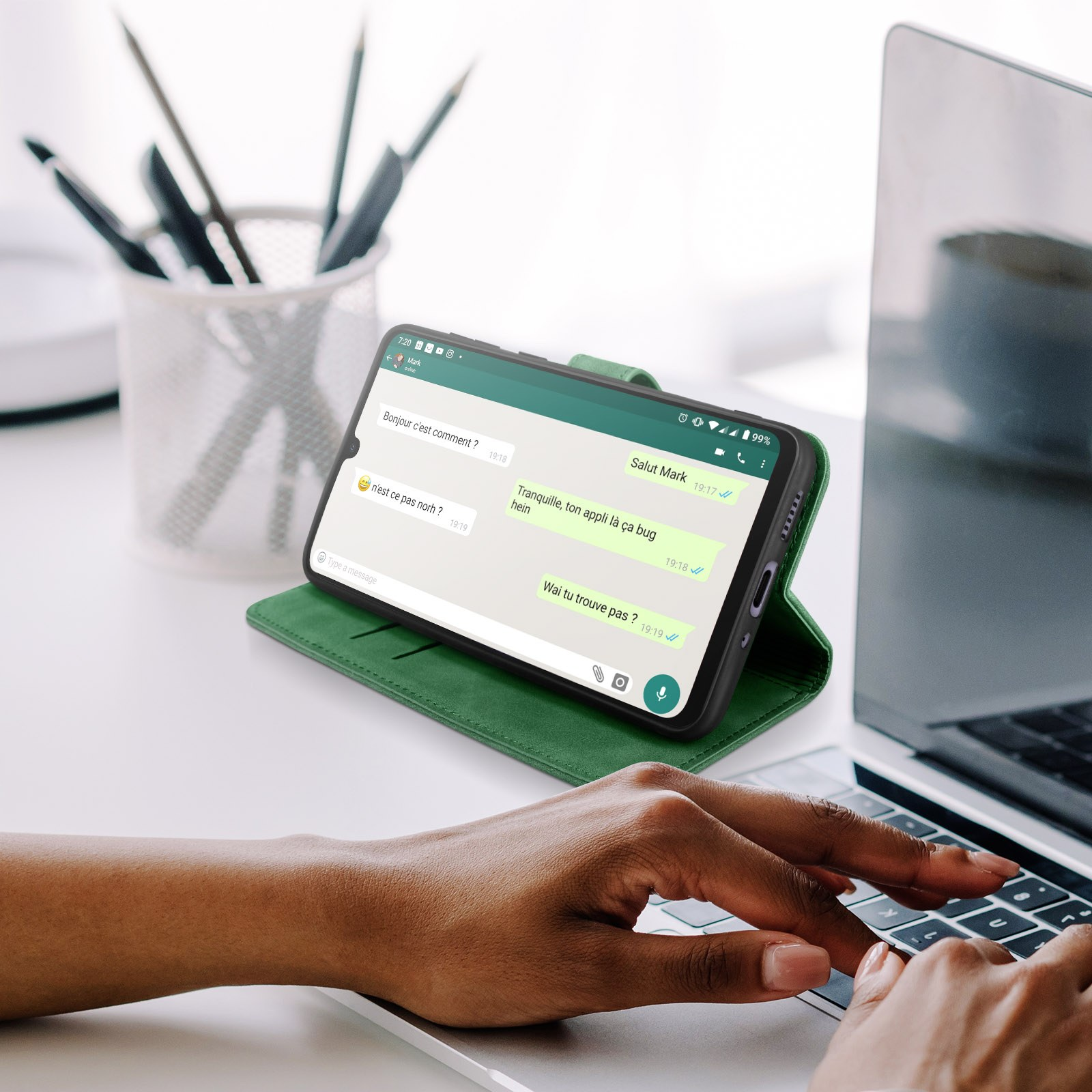 Person tippt auf einer Tastatur, Telefon auf grüner Hülle zeigt Chat an.