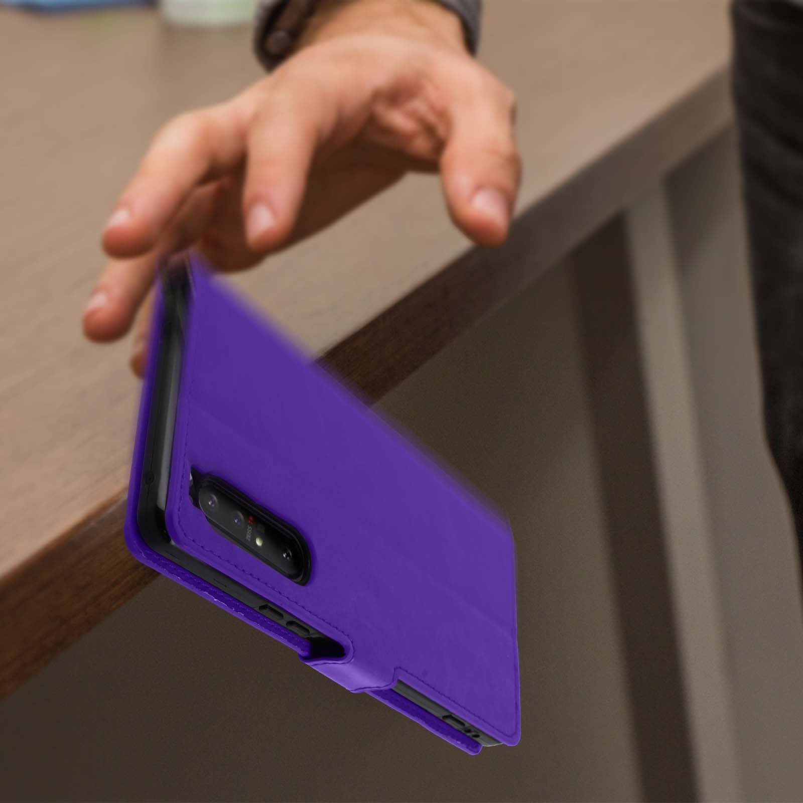 Mano che lascia cadere una custodia viola per telefono. Un tavolo di legno sullo sfondo.