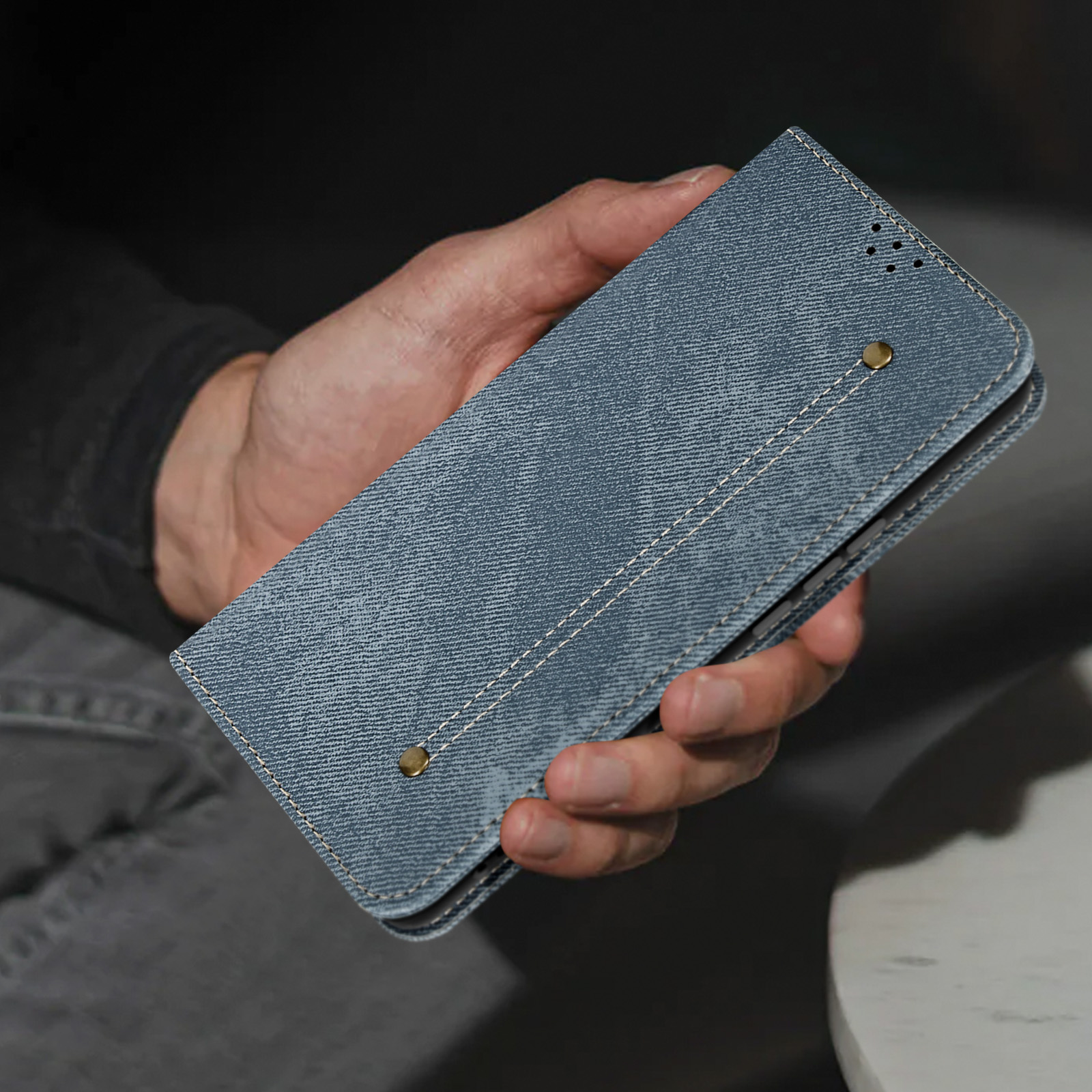 Mano che tiene una custodia in denim. Due bottoni in bronzo sono visibili.