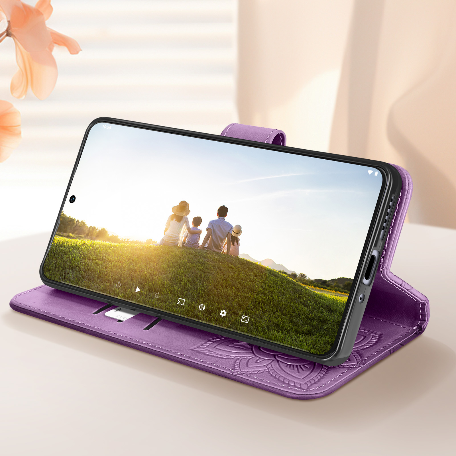 Custodia in pelle viola con un telefono che mostra una famiglia su una collina verde, con sfondo floreale.