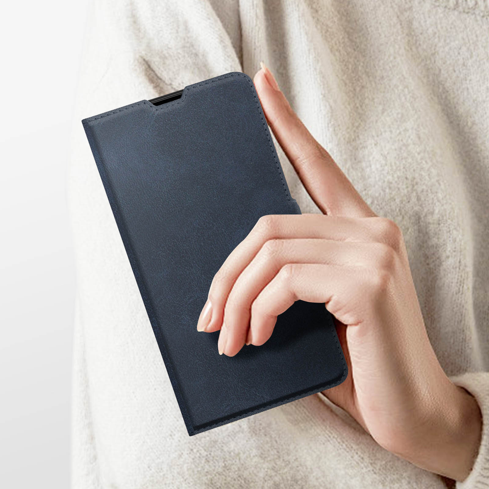 La mano di una persona che tiene una custodia per telefono in pelle blu navy, contro un maglione beige chiaro.