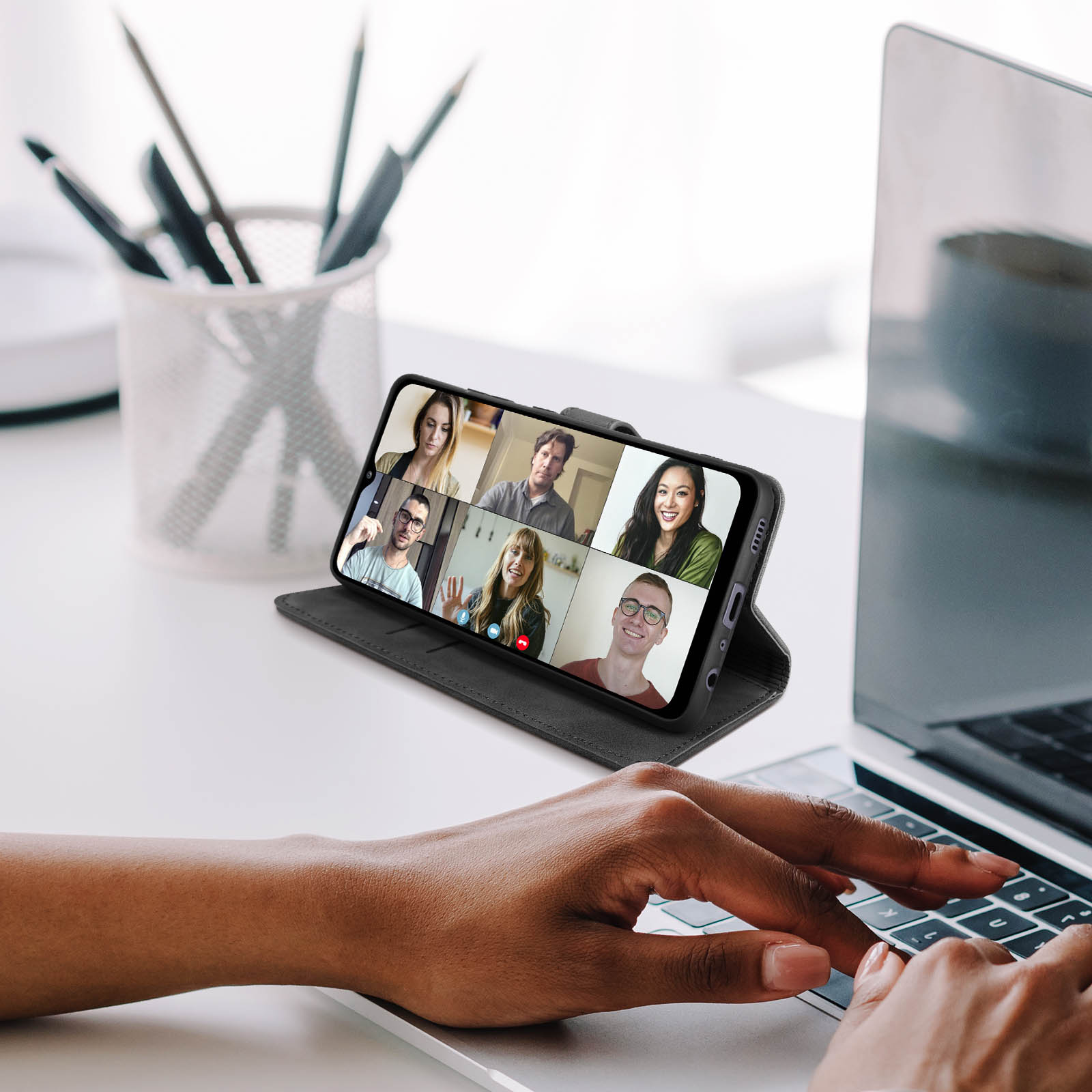 Una persona usa un laptop con un telefono che mostra una videochiamata.