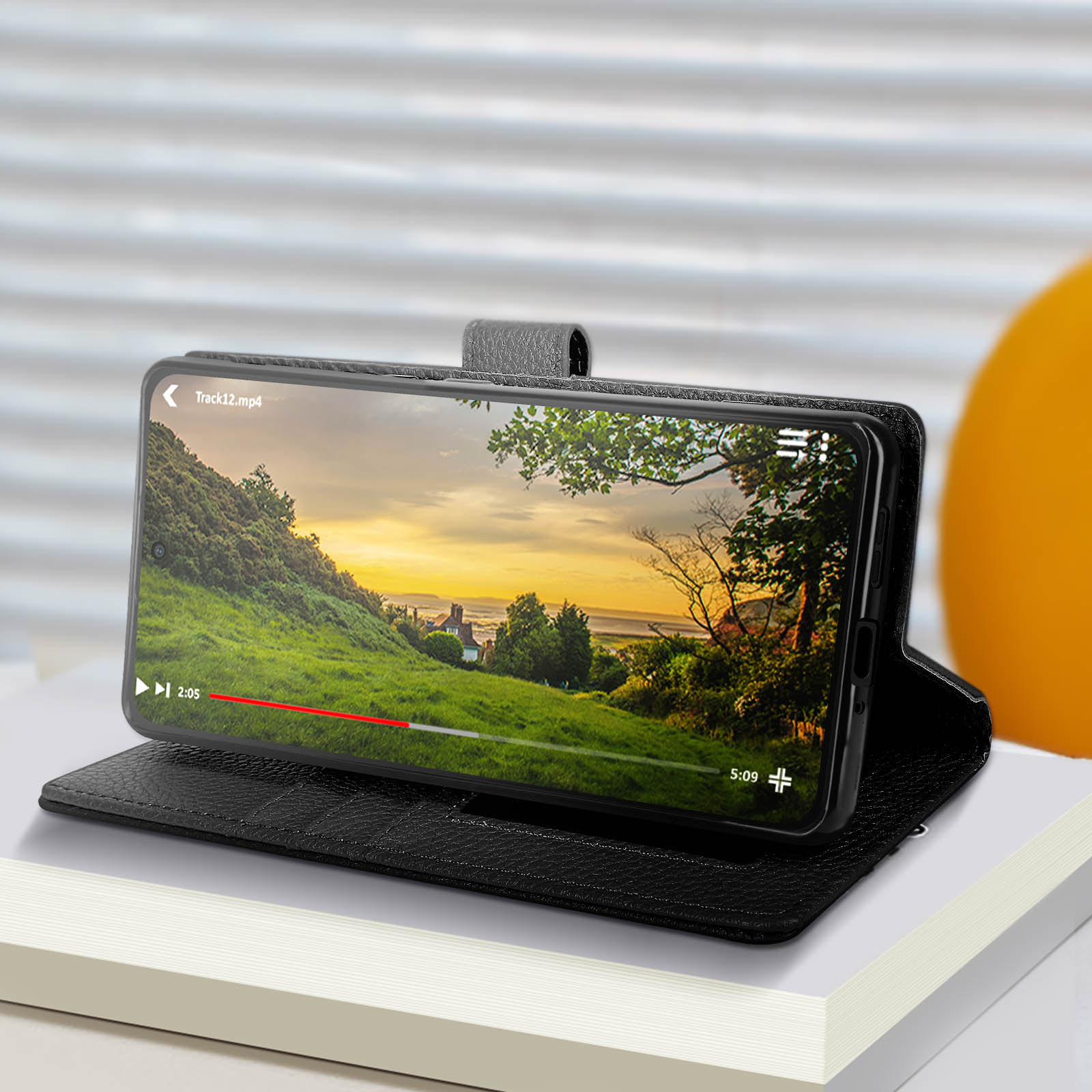 Telefono in una custodia che riproduce un video. La custodia è su un libro. Campo verde nel video.