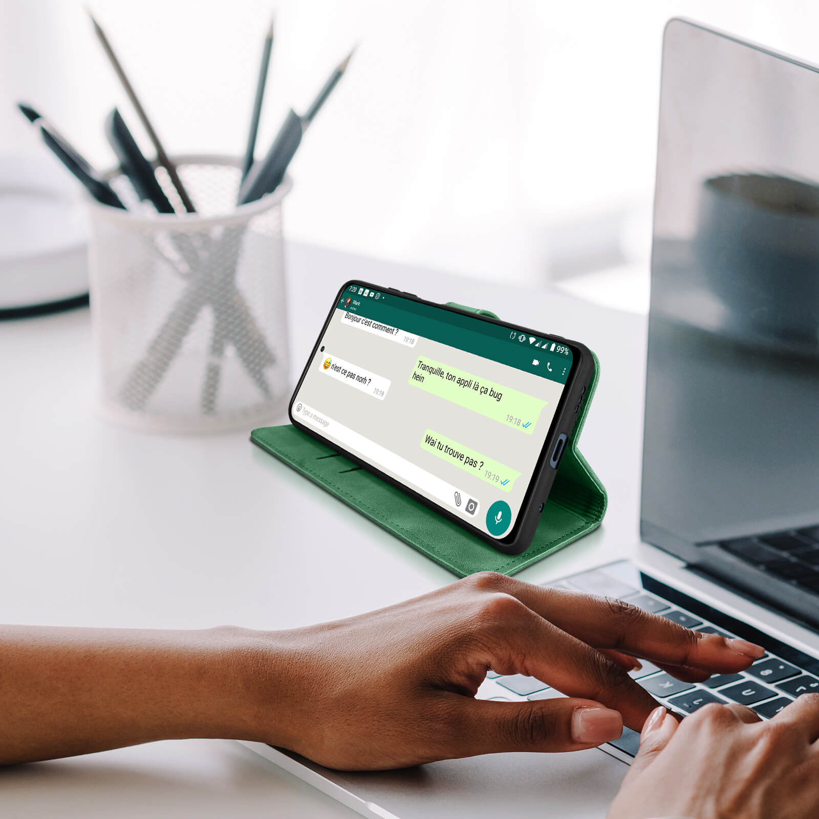 Un telefono con una custodia verde è su una scrivania bianca. Lo schermo mostra un'interfaccia di chat.