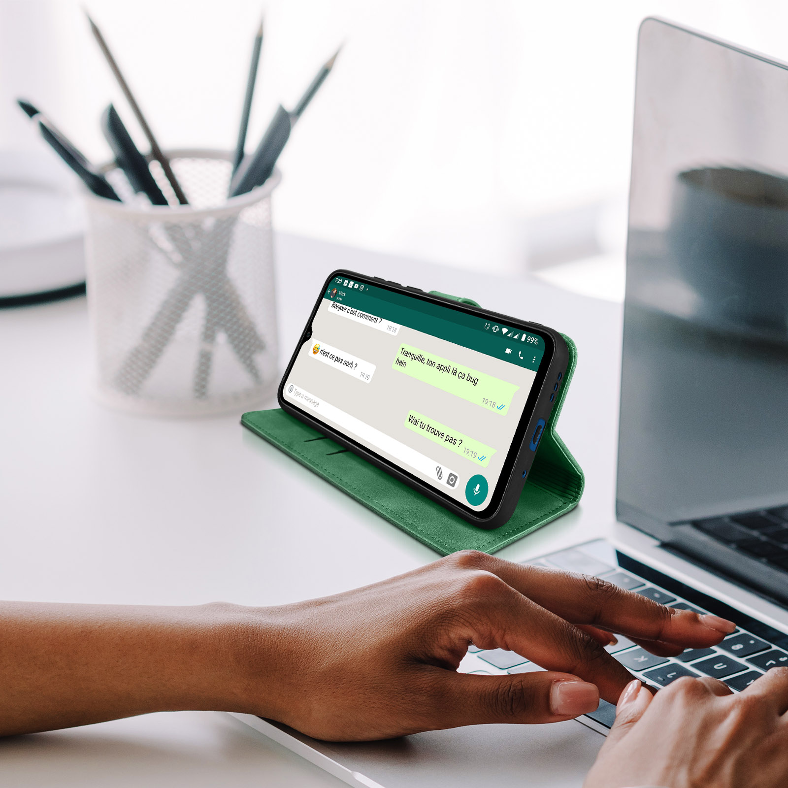 Custodia verde con telefono che mostra schermo chat su tavolo con laptop.