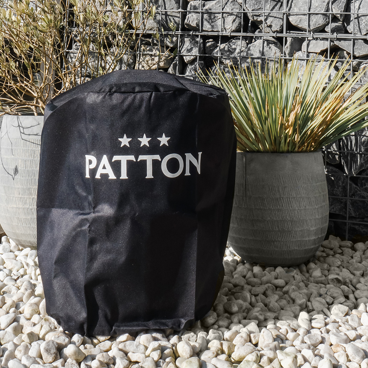 A black outdoor grill cover with a white logo and three stars, placed on a stone patio.