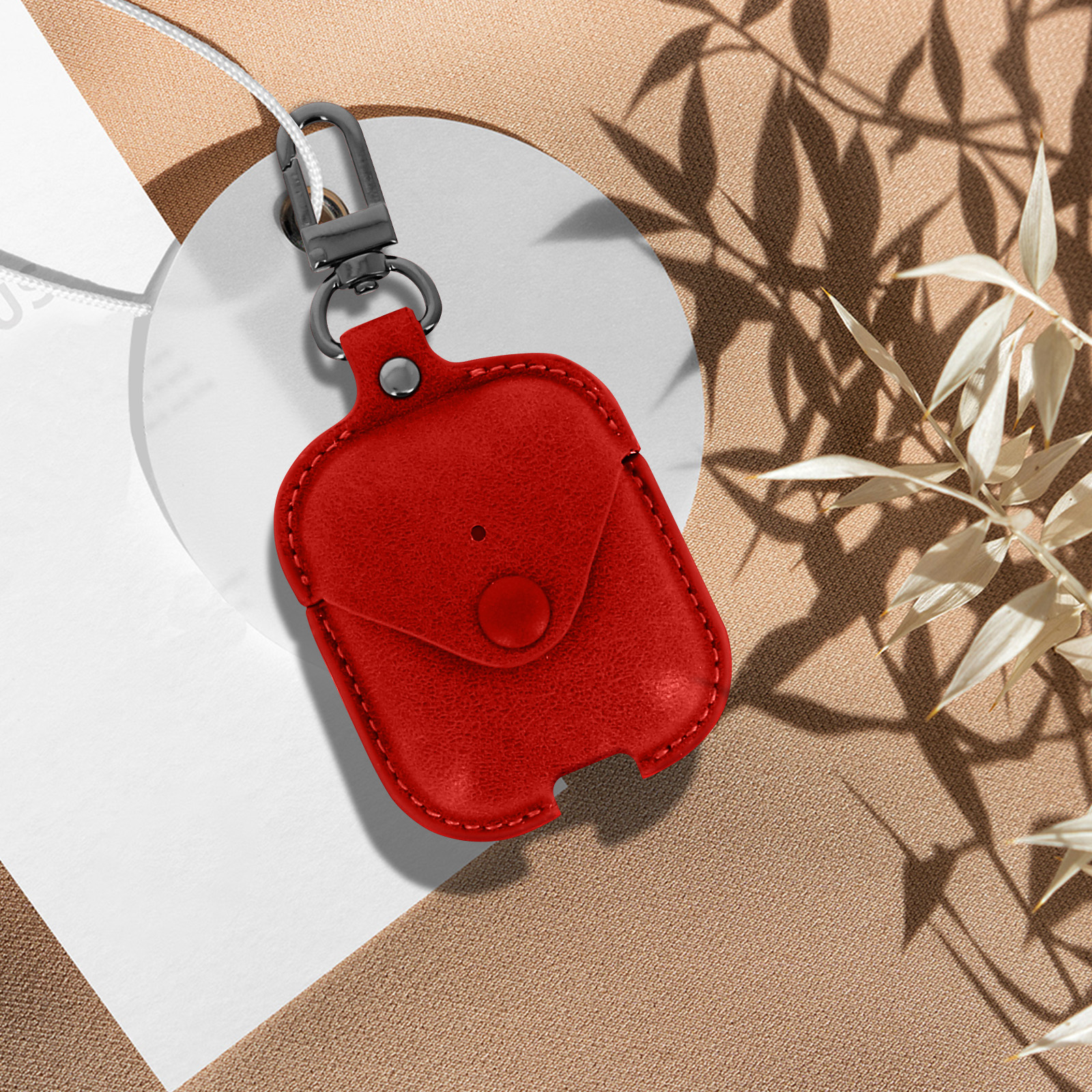 Funda roja de AirPods sobre una superficie blanca, con gancho gris y correa blanca.