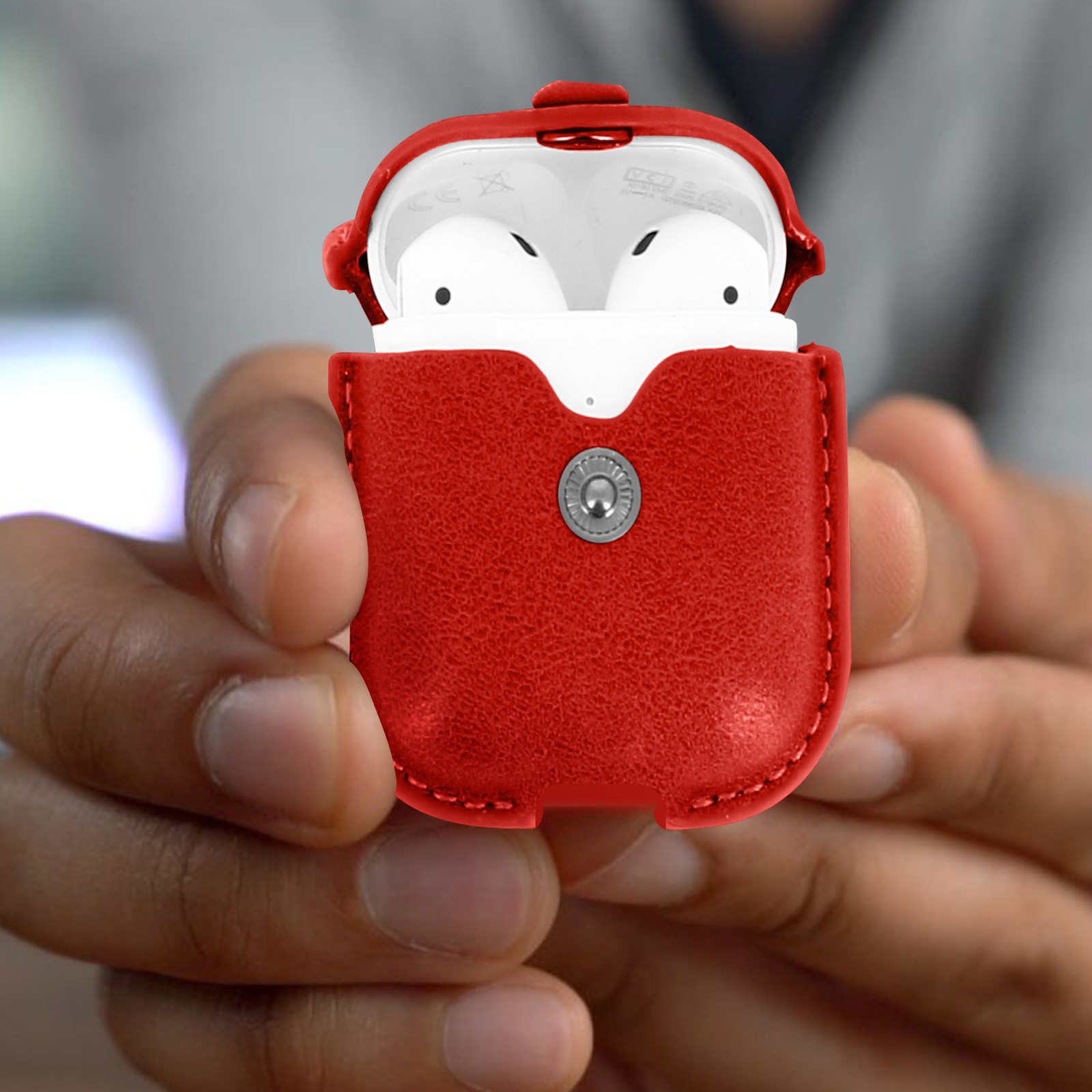 Funda roja para Airpods, abierta. Airpods blancos dentro. Sostenida en dos manos.