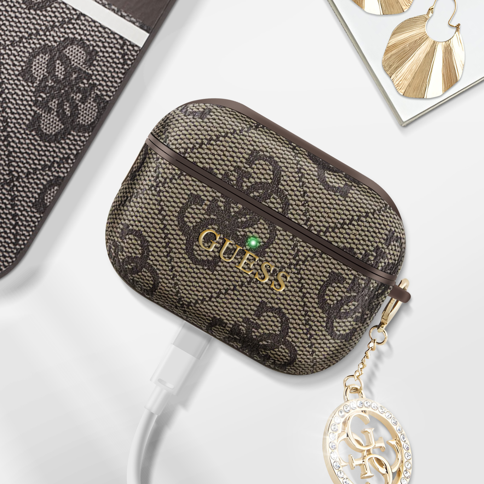 Una custodia per AirPods Guess marrone con un ciondolo dorato e un cavo di ricarica.