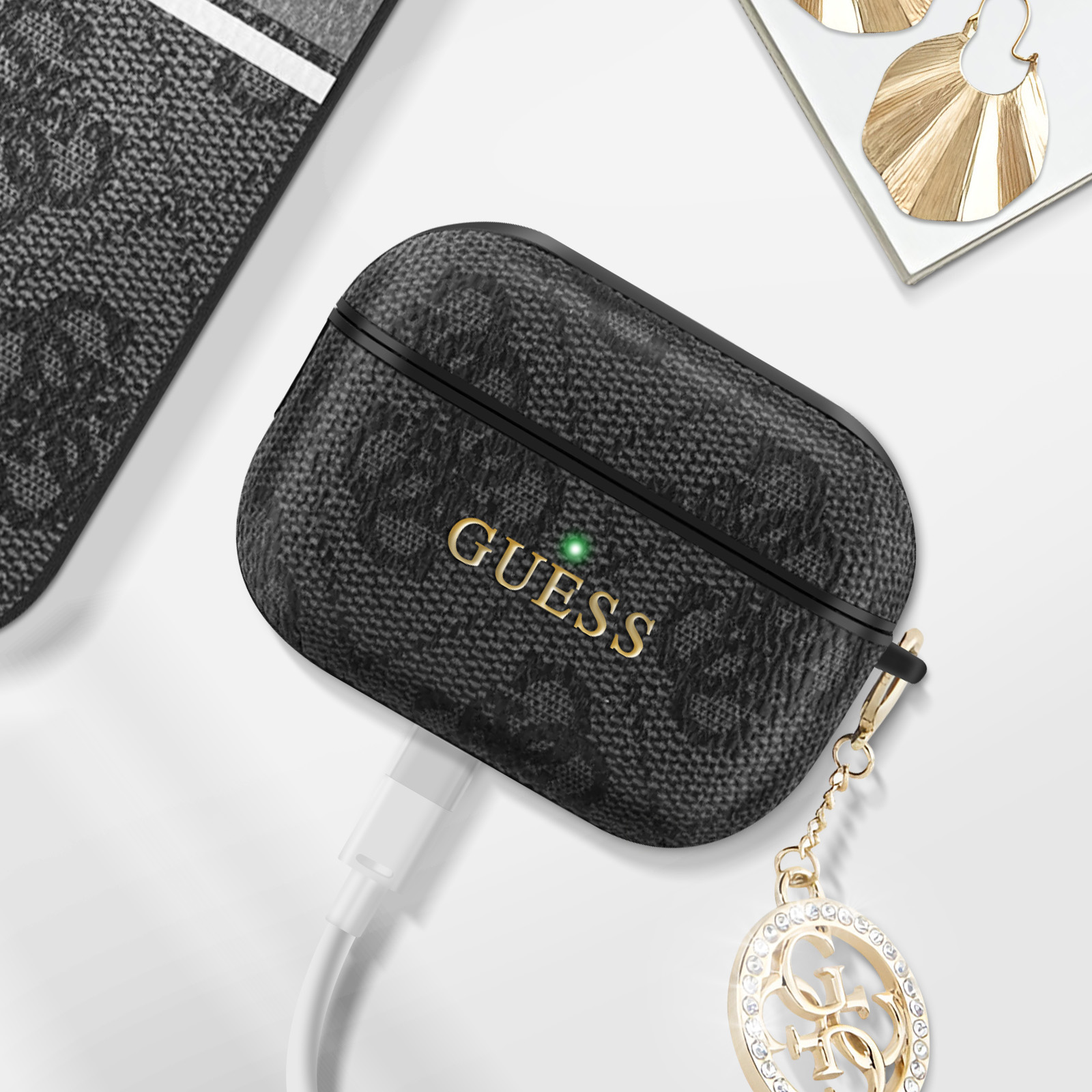 Custodia per AirPods nera e grigia con logo e ciondolo Guess. Cavo di ricarica bianco collegato.