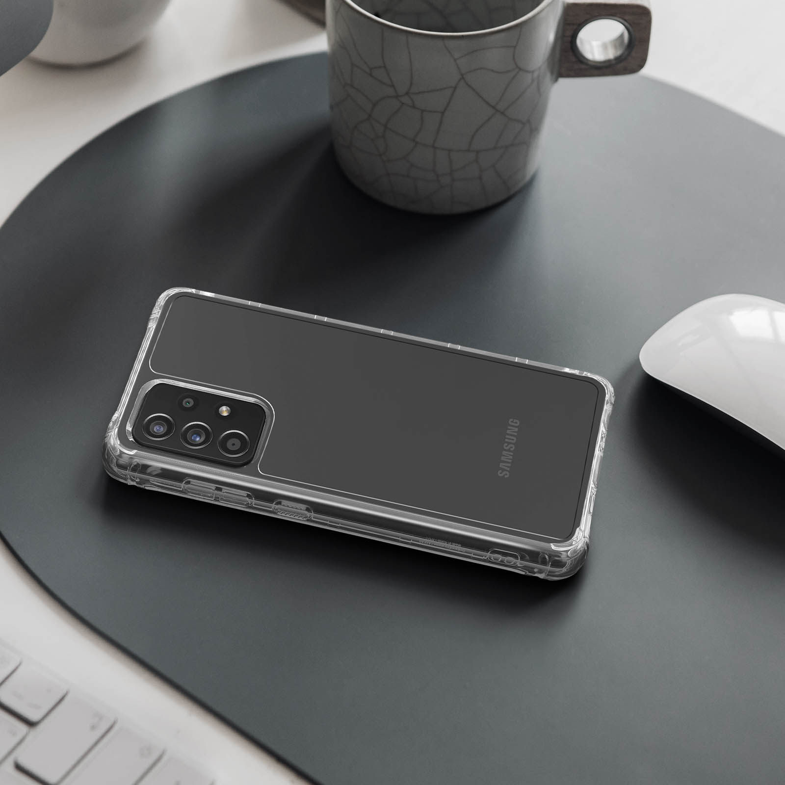 Telefono Samsung in custodia trasparente su tappetino grigio scuro. Tazza e mouse.