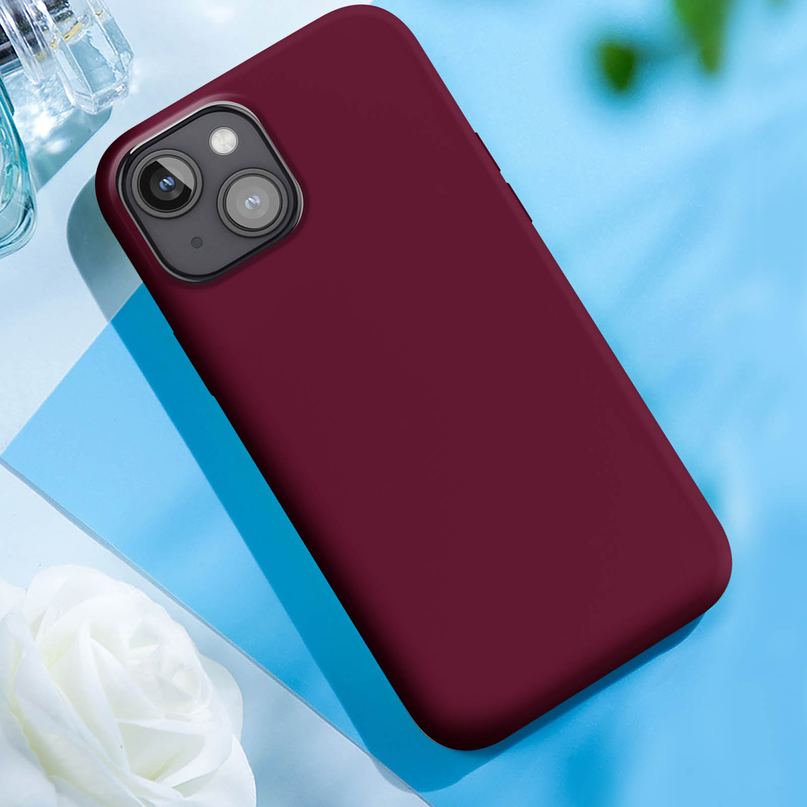Custodia rossa per telefono su superficie blu con fiore bianco e profumo.
