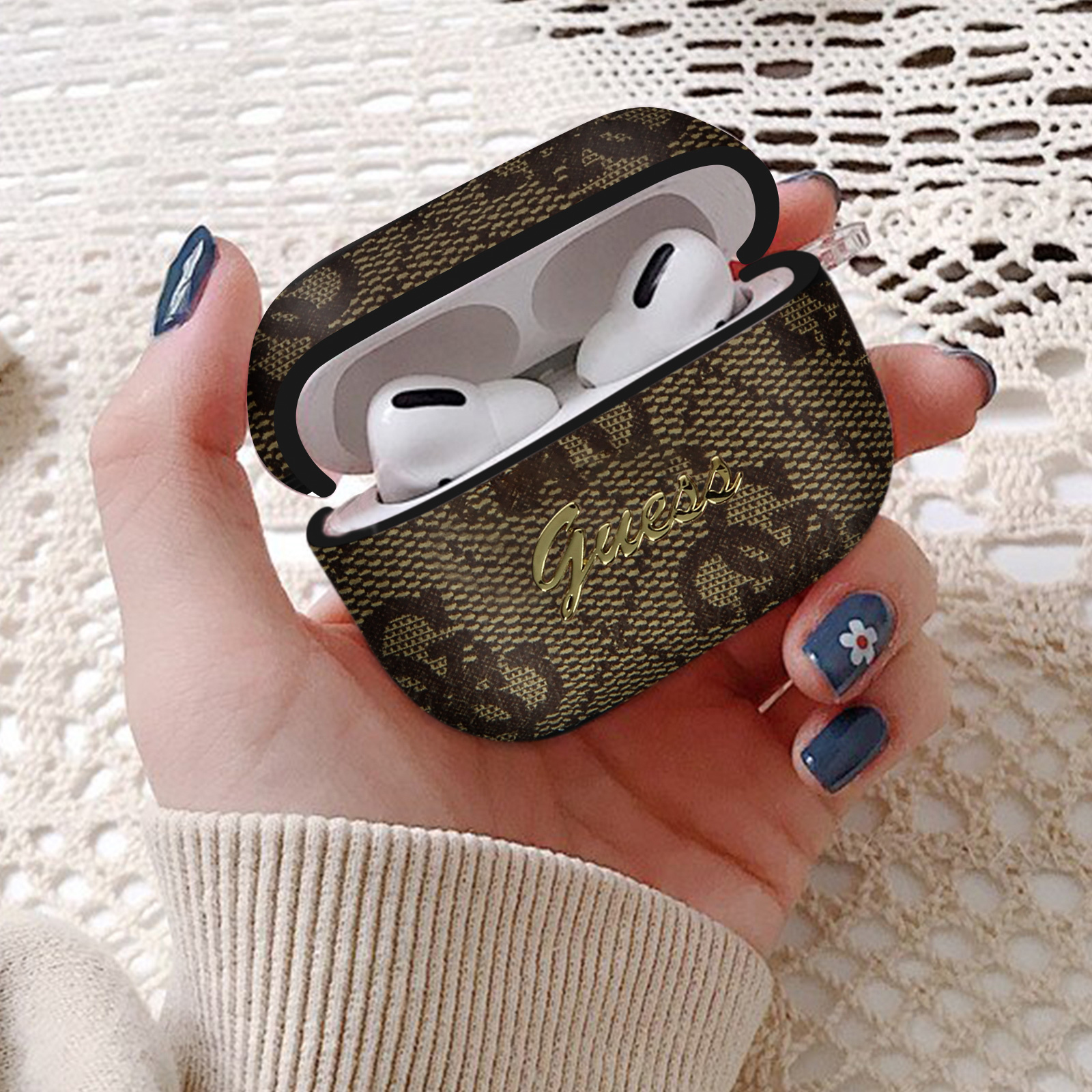 Una mano sosteniendo un estuche de auriculares abierto con 'Guess' en él. Los auriculares son visibles.