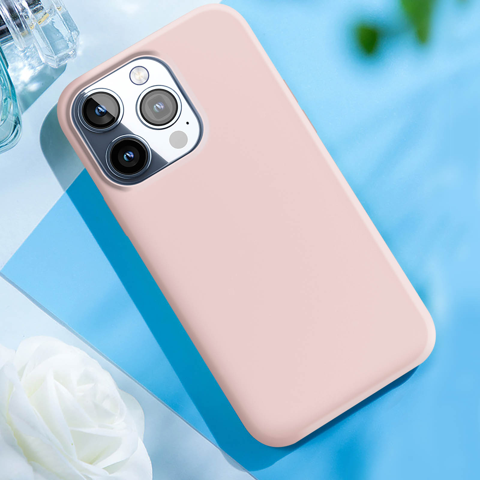 Custodia per telefono rosa su una superficie blu. Un fiore bianco e un flacone di profumo sono sullo sfondo.