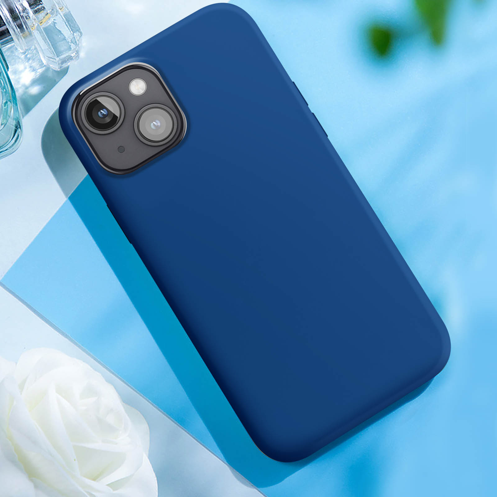 Una custodia blu per telefono su una superficie azzurra. Sono presenti anche un fiore bianco e un flacone di profumo.