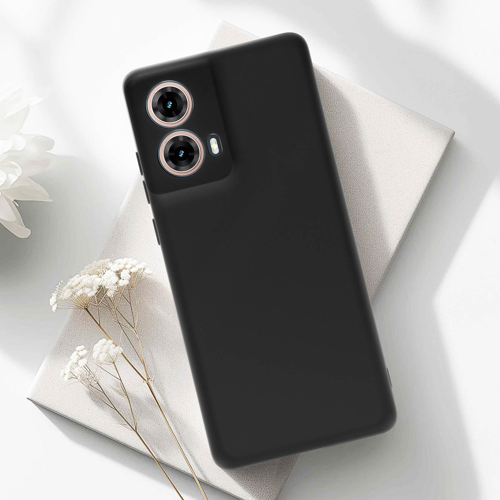 Custodia nera per telefono con ritagli per fotocamera su superficie bianca, con fiori bianchi.