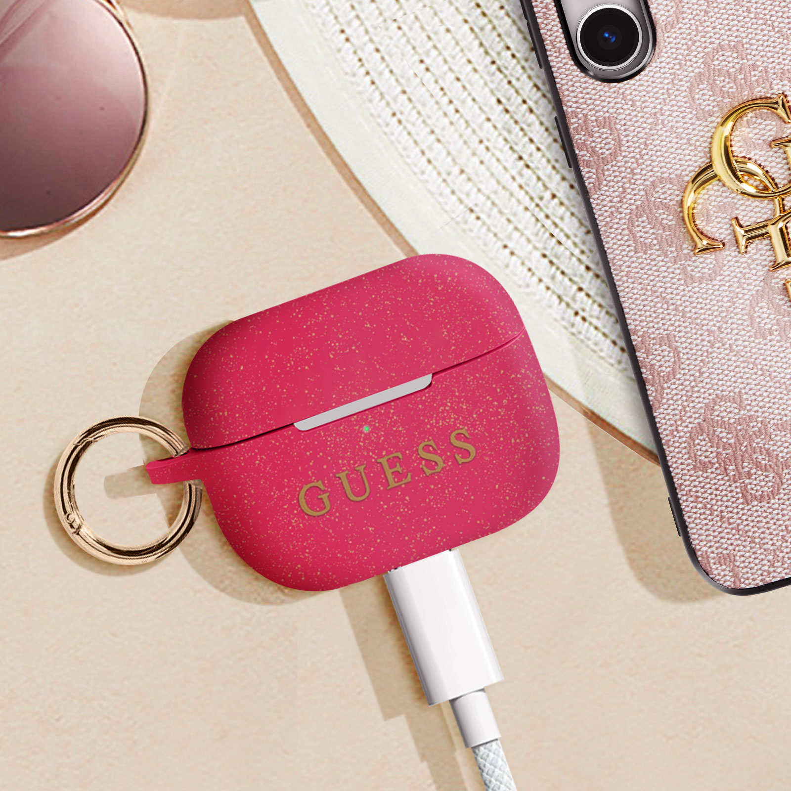 Funda roja para AirPods con anillo dorado y marca Guess. Cable de carga blanco.