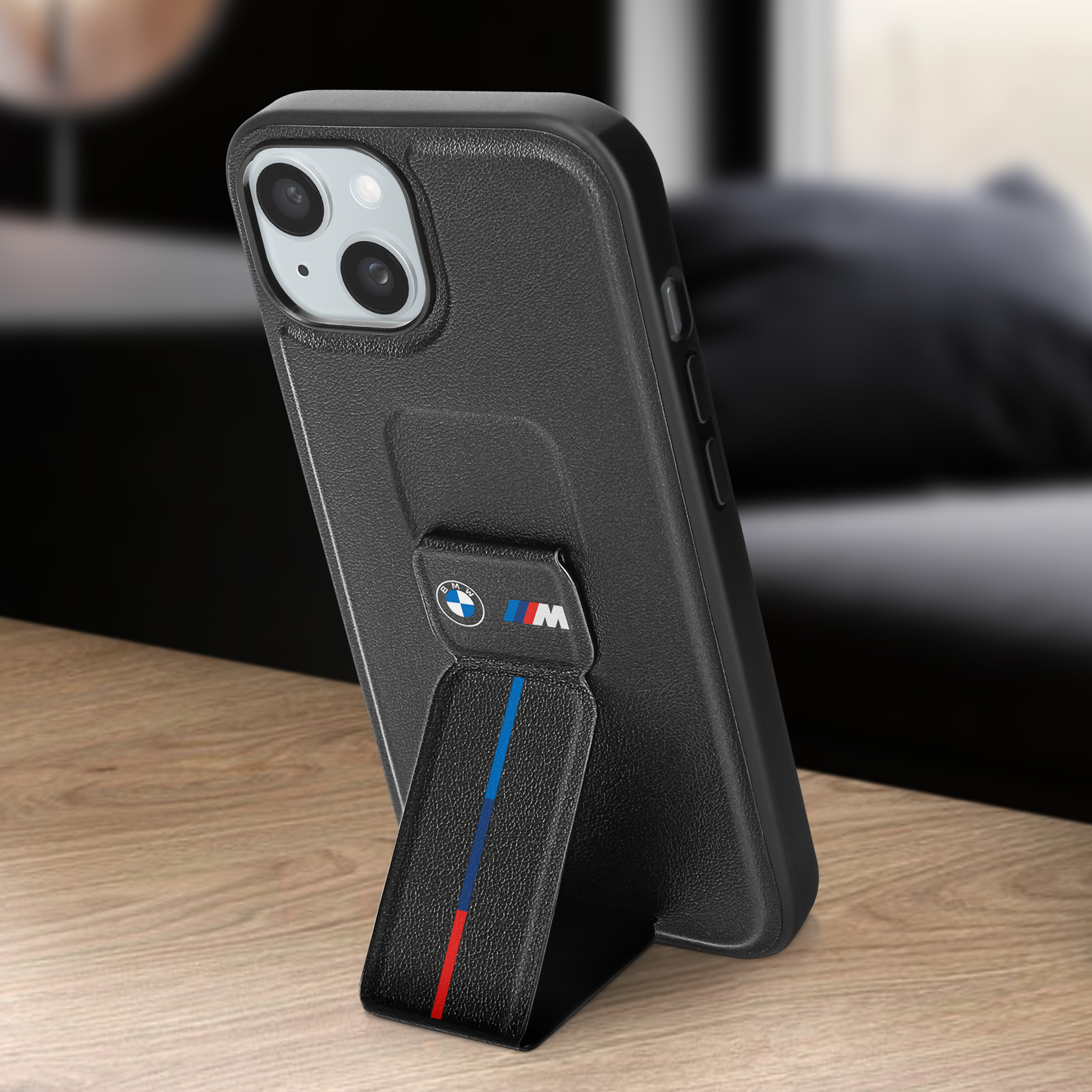Telefono nero con supporto. Il supporto ha strisce rosse e blu e un logo BMW. Tavolo di legno.