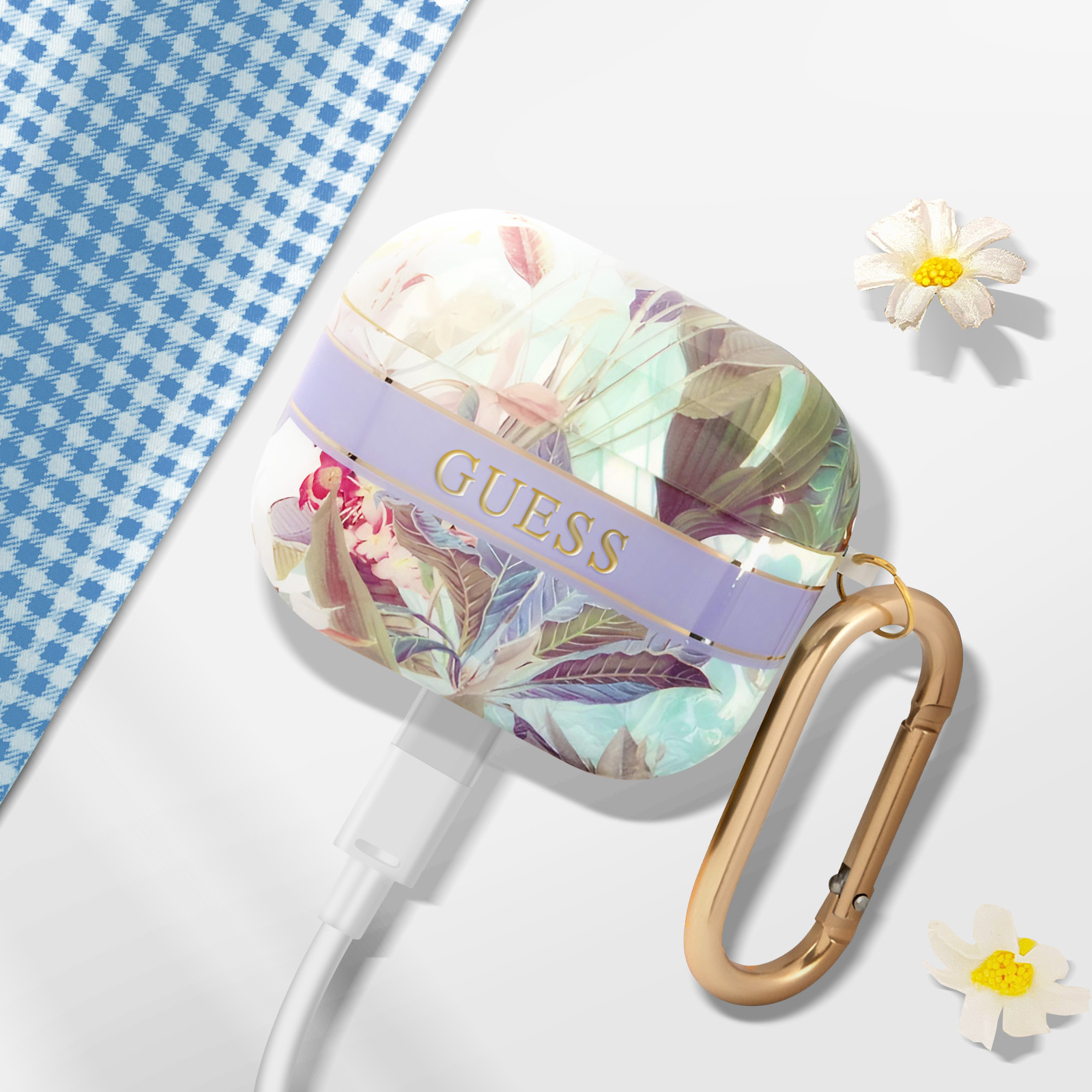 Funda floral Guess para AirPods con herrajes dorados, cable blanco y margaritas sobre una superficie blanca con fondo a cuadros azules.