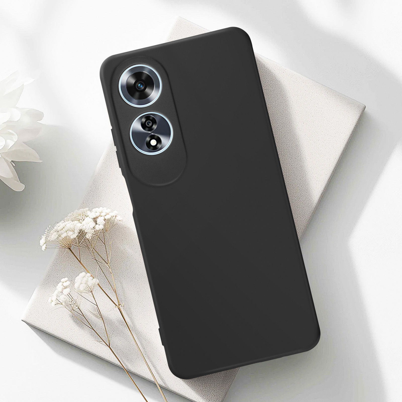 Custodia nera con modulo fotocamera visibile. Poggia su una superficie bianca con fiori.