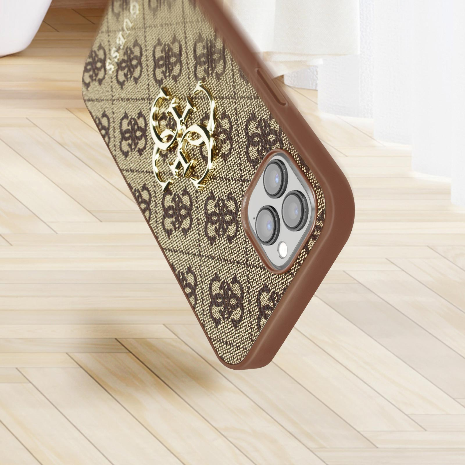 Custodia per telefono con sfondo marrone e logo Guess. Emblema dorato sul telefono.