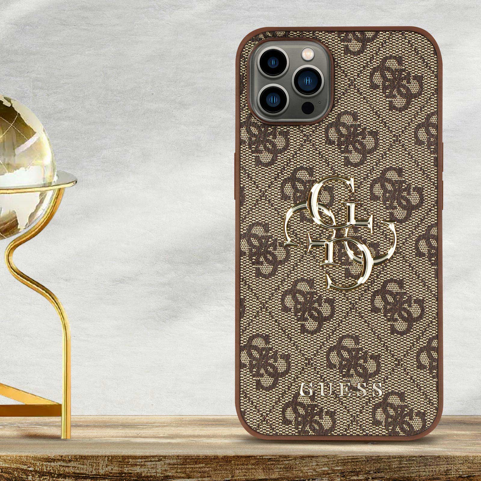Una custodia per telefono con un motivo Guess marrone, con un logo Guess dorato. Si trova su una superficie di legno.