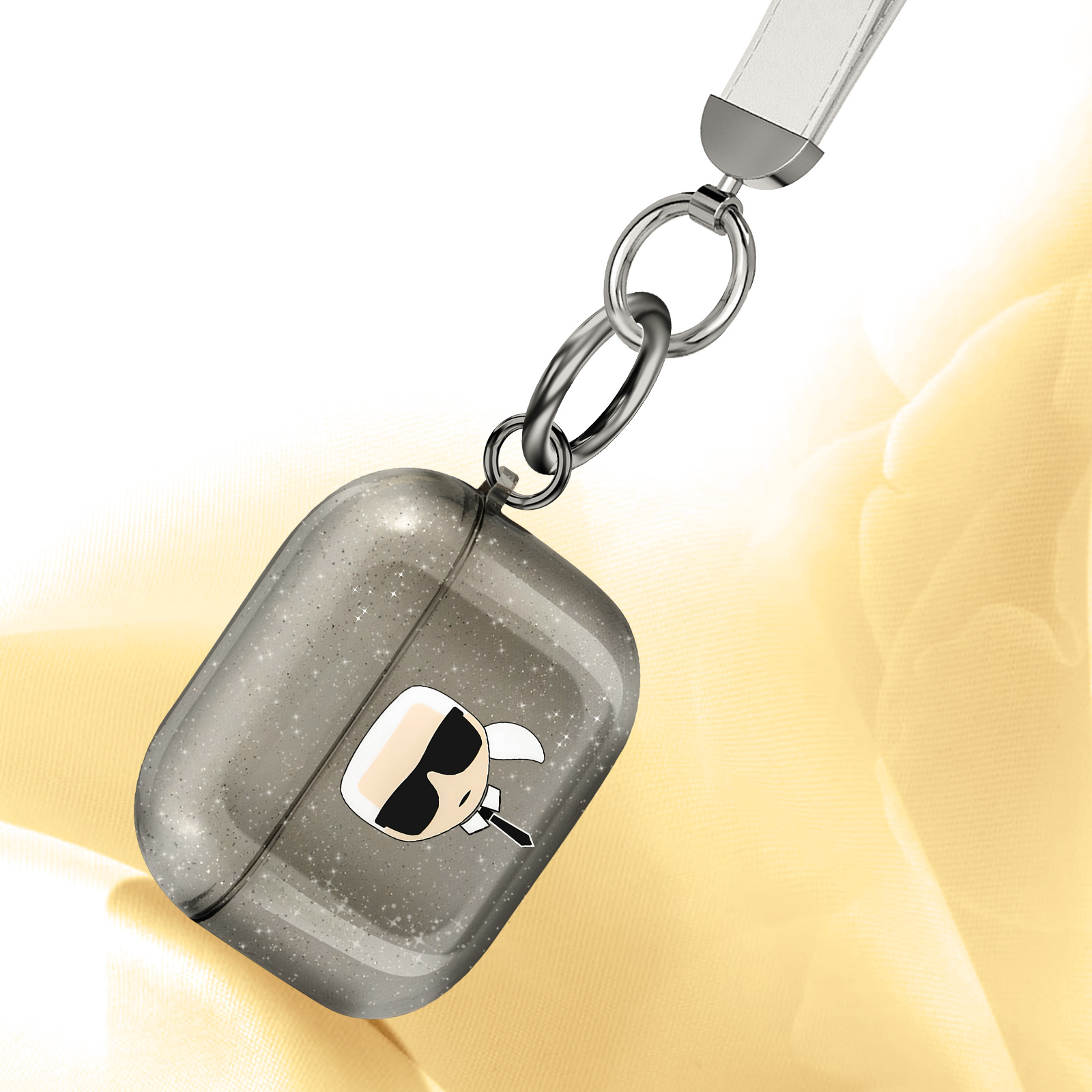 Funda gris para AirPod con diseño de Karl Lagerfeld, colgando. Fondo dorado.