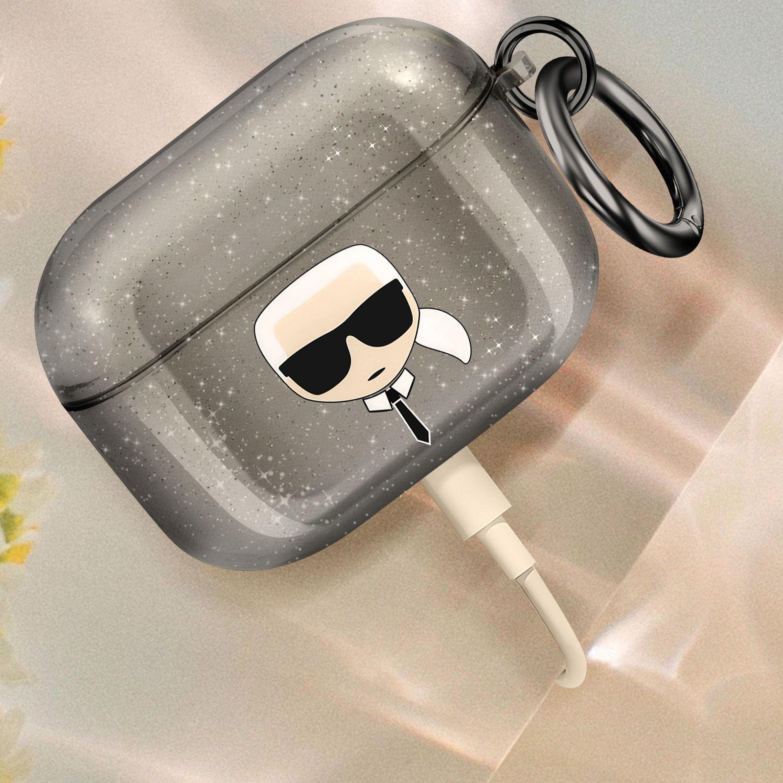 Funda AirPods plateada con purpurina y diseño Karl Lagerfeld. Fondo blanco.