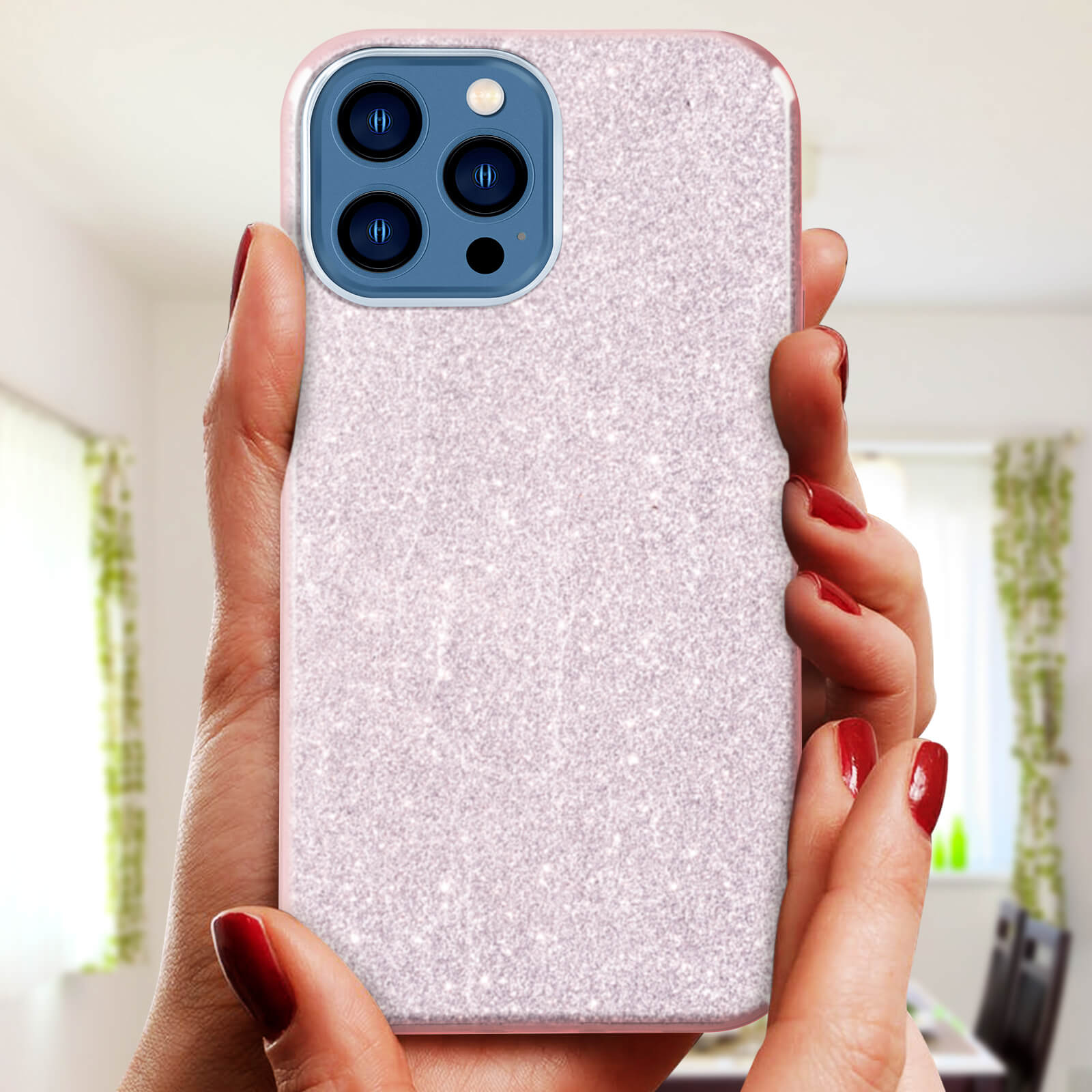Mani che tengono un telefono in una custodia glitterata. Le mani hanno lo smalto rosso. Una finestra è sullo sfondo.