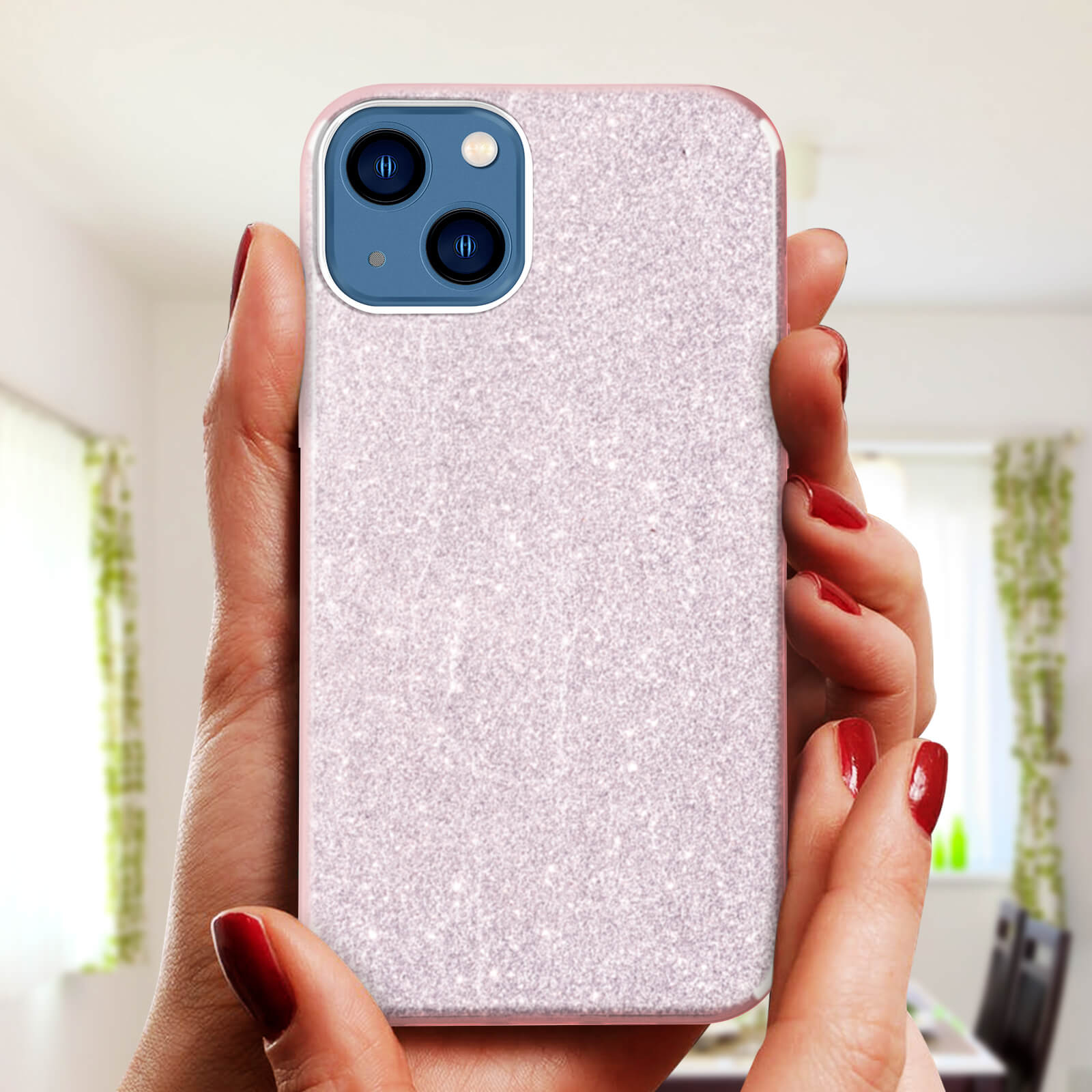 Mani che tengono una custodia rosa glitterata. Stanza con sfondo finestra.
