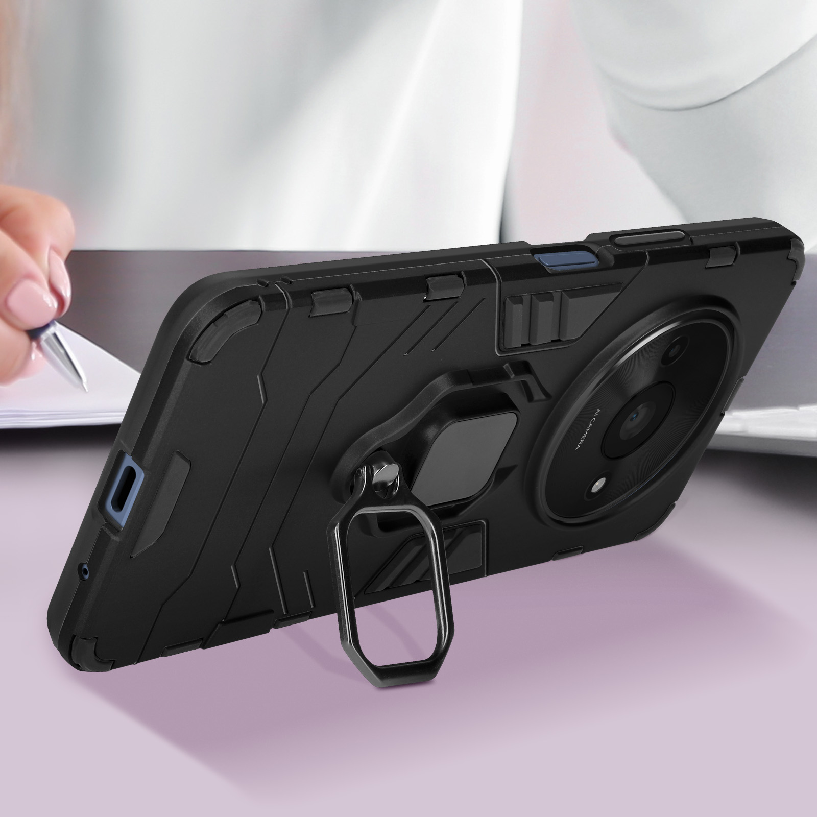 Schwarze Handyhülle mit Ringständer auf einem Tisch. Eine Person schreibt im Hintergrund.