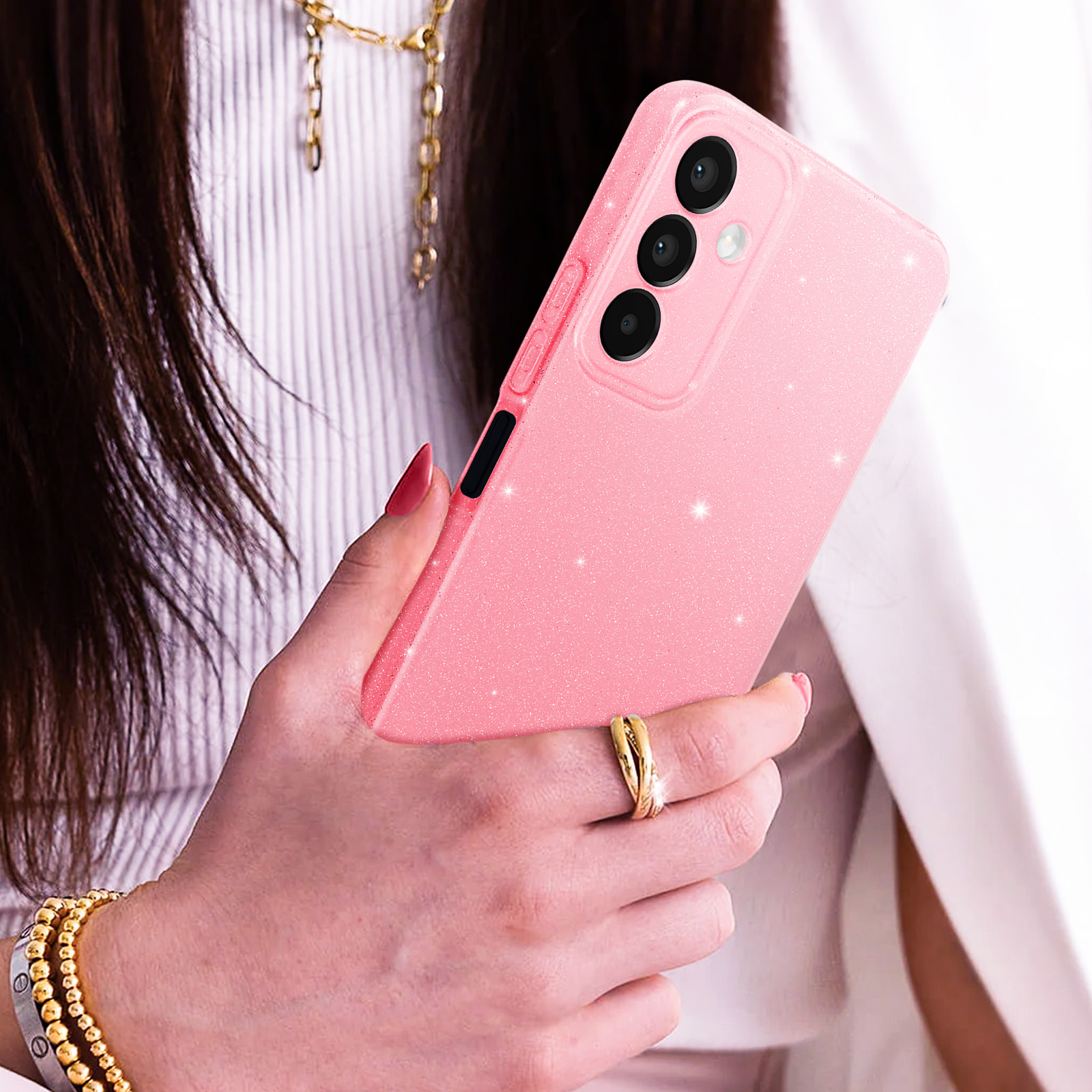 Custodia rosa per telefono con brillantini. Mano che tiene il telefono, anello e bracciale d'oro.