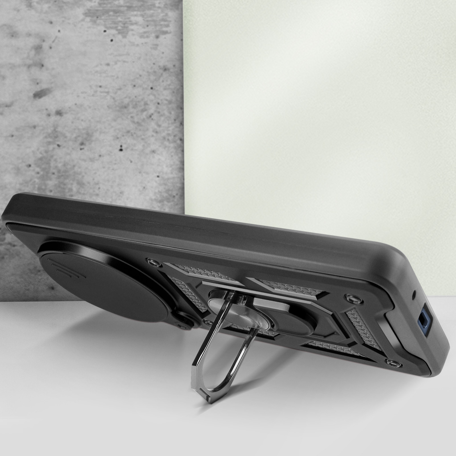 Custodia nera per telefono con supporto ad anello, vista laterale. Sfondo grigio e bianco.