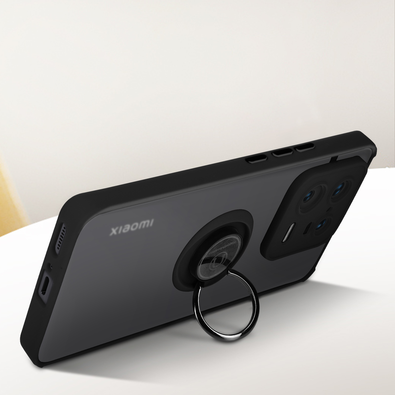 Telefono nero con custodia con supporto ad anello, su un tavolo. Logo Xiaomi visibile.