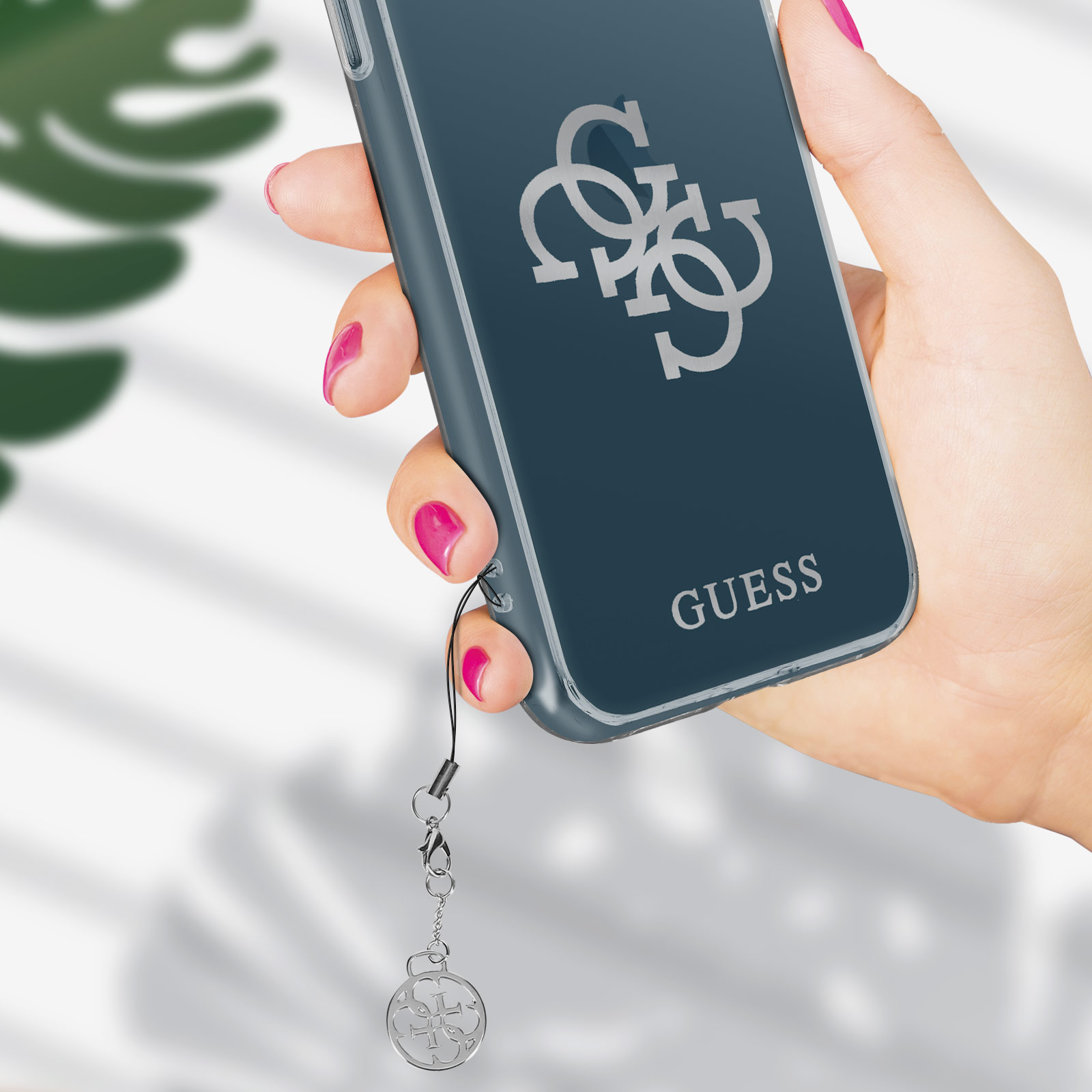 Mano che tiene un telefono con il logo Guess. Il telefono è in una custodia trasparente.