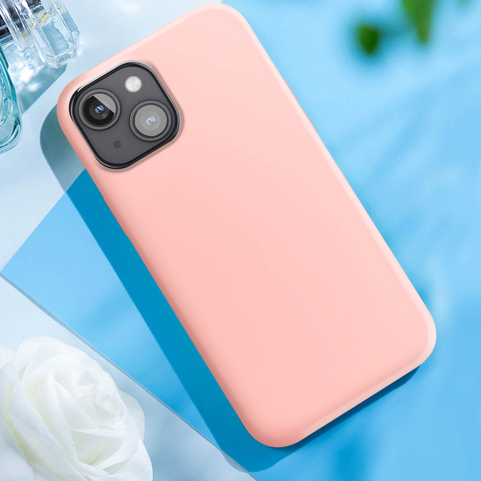 Custodia per telefono rosa su una superficie blu con fiore bianco e profumo.