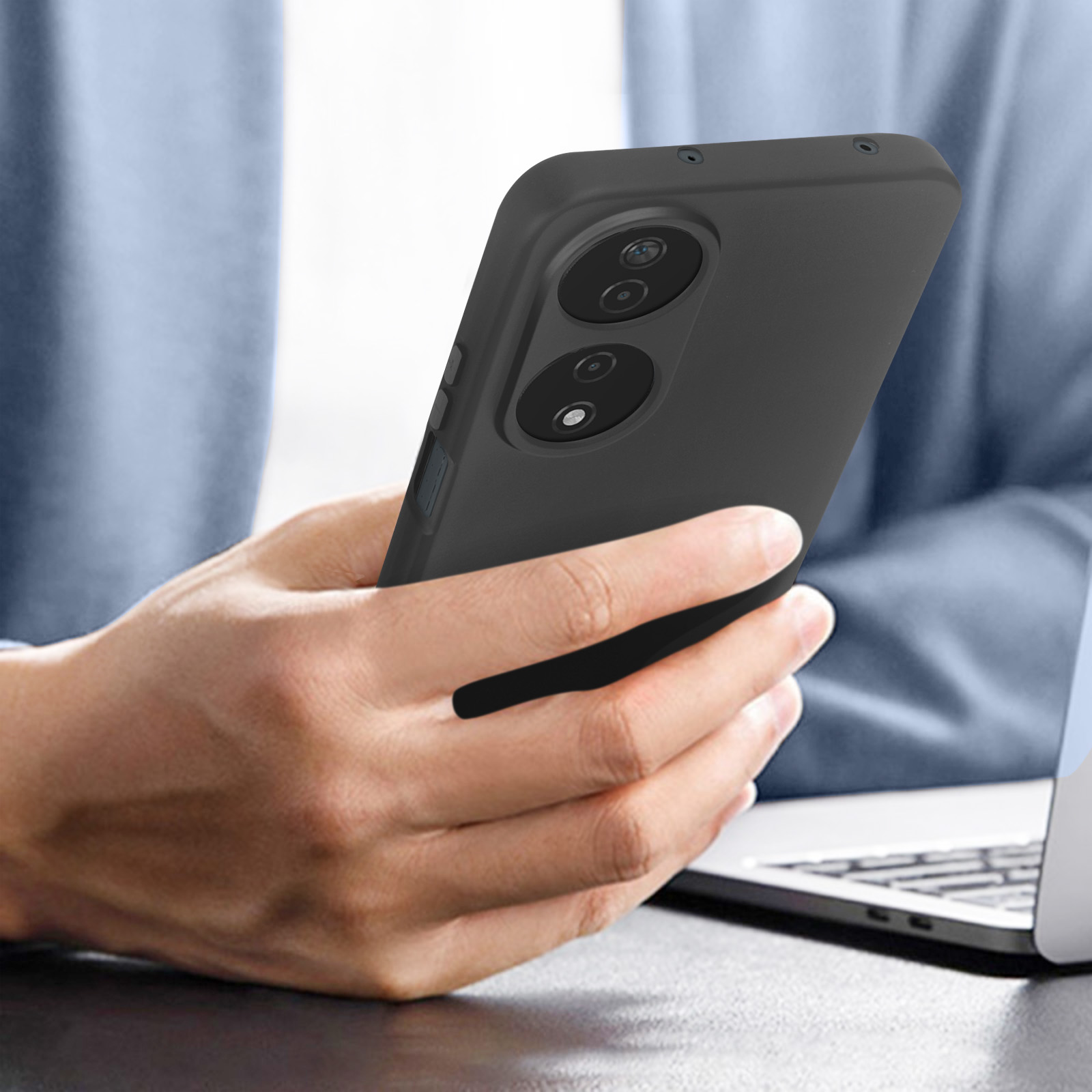 Mano che tiene un telefono nero con fotocamera. Un laptop sullo sfondo.