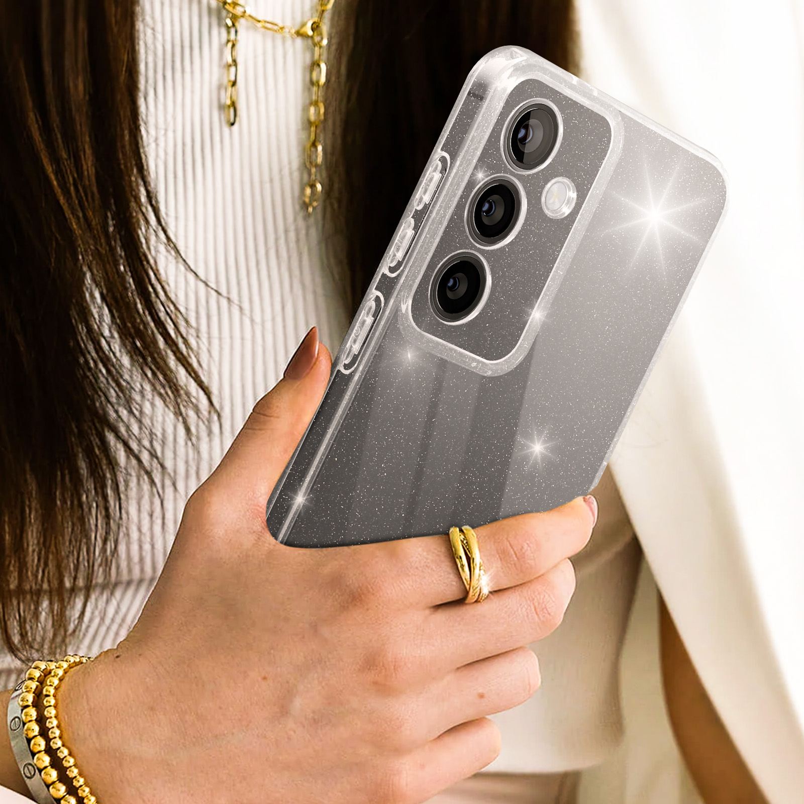 Donna con telefono in custodia scintillante. Indossa un braccialetto e un anello d'oro.