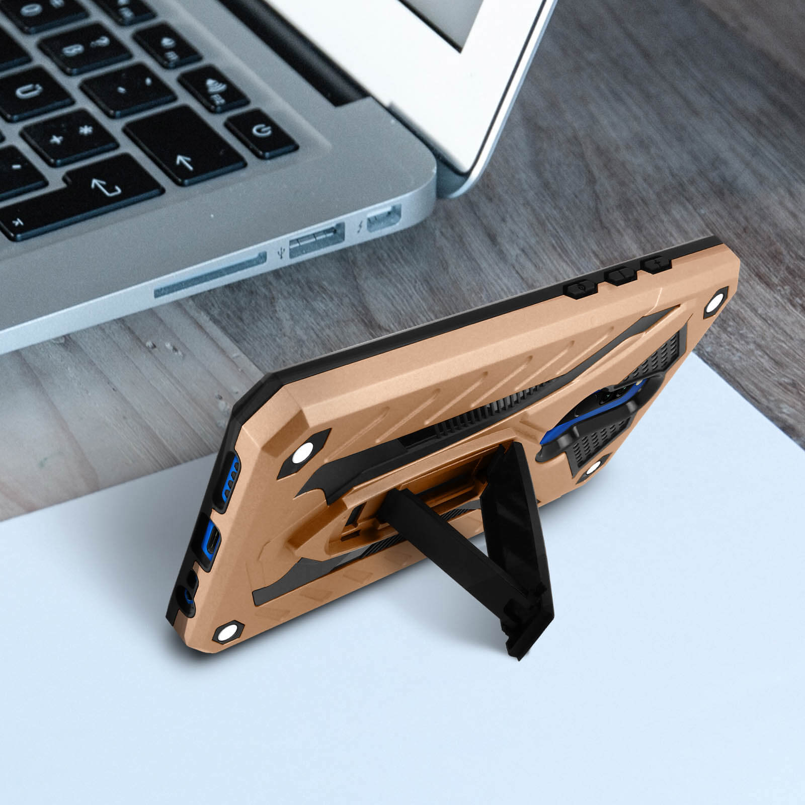 Una custodia per telefono, appoggiata, su una superficie. Un laptop è sullo sfondo. La custodia è oro e nera.