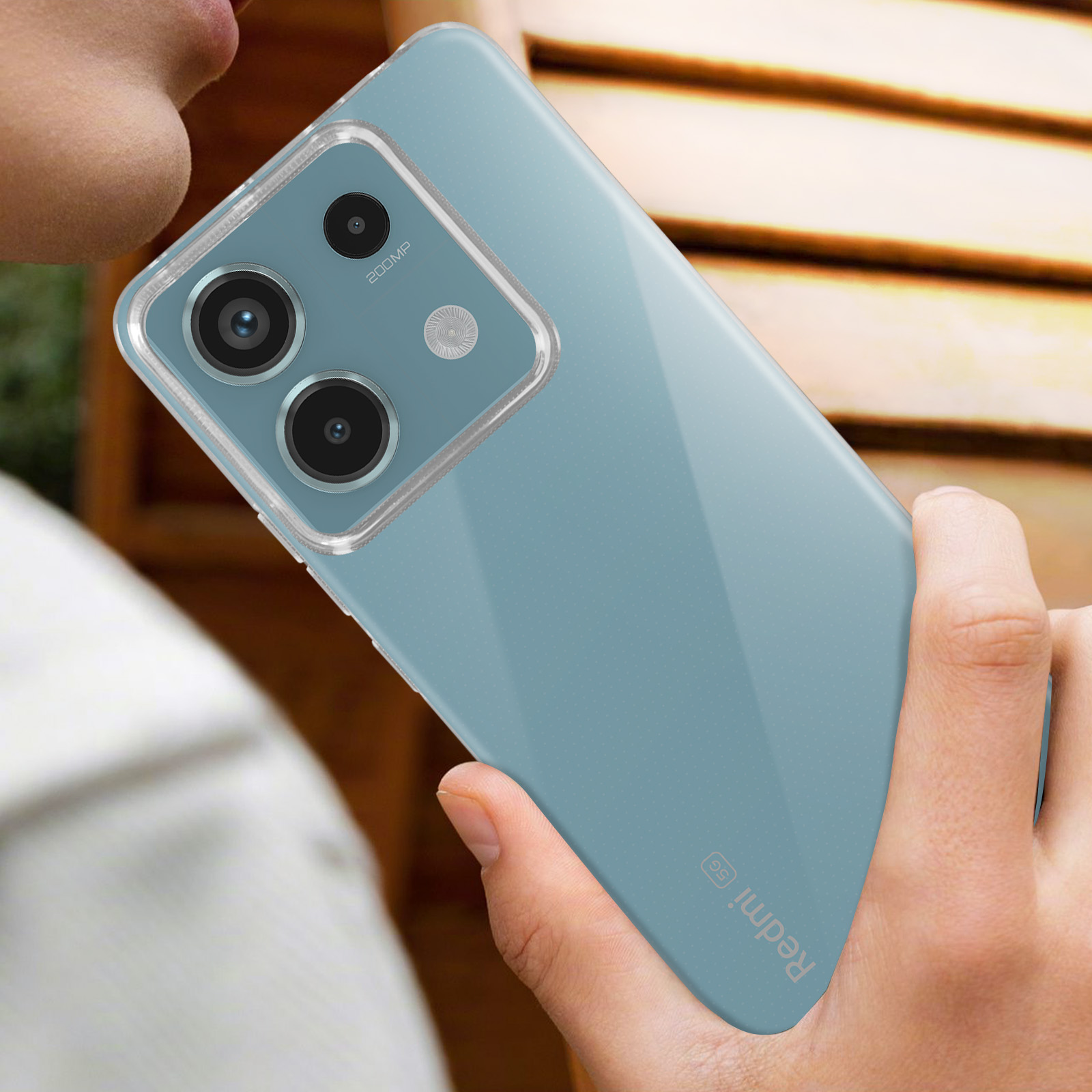 Una persona che tiene in mano un telefono. Il telefono è blu con una custodia trasparente. La fotocamera è visibile.