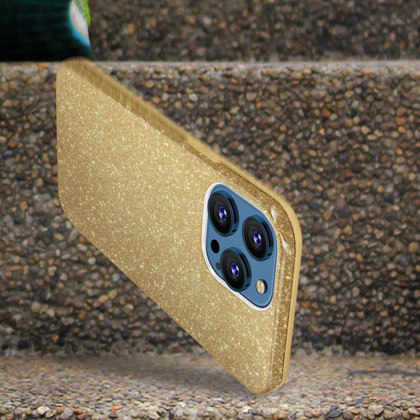 Custodia per telefono glitterata dorata su una scala di pietra. La custodia ha una configurazione a tripla fotocamera.