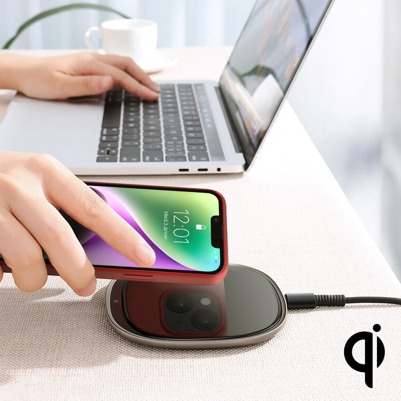 Un telefono è posizionato su un caricatore wireless. Una persona tiene il telefono. Un laptop è sullo sfondo.